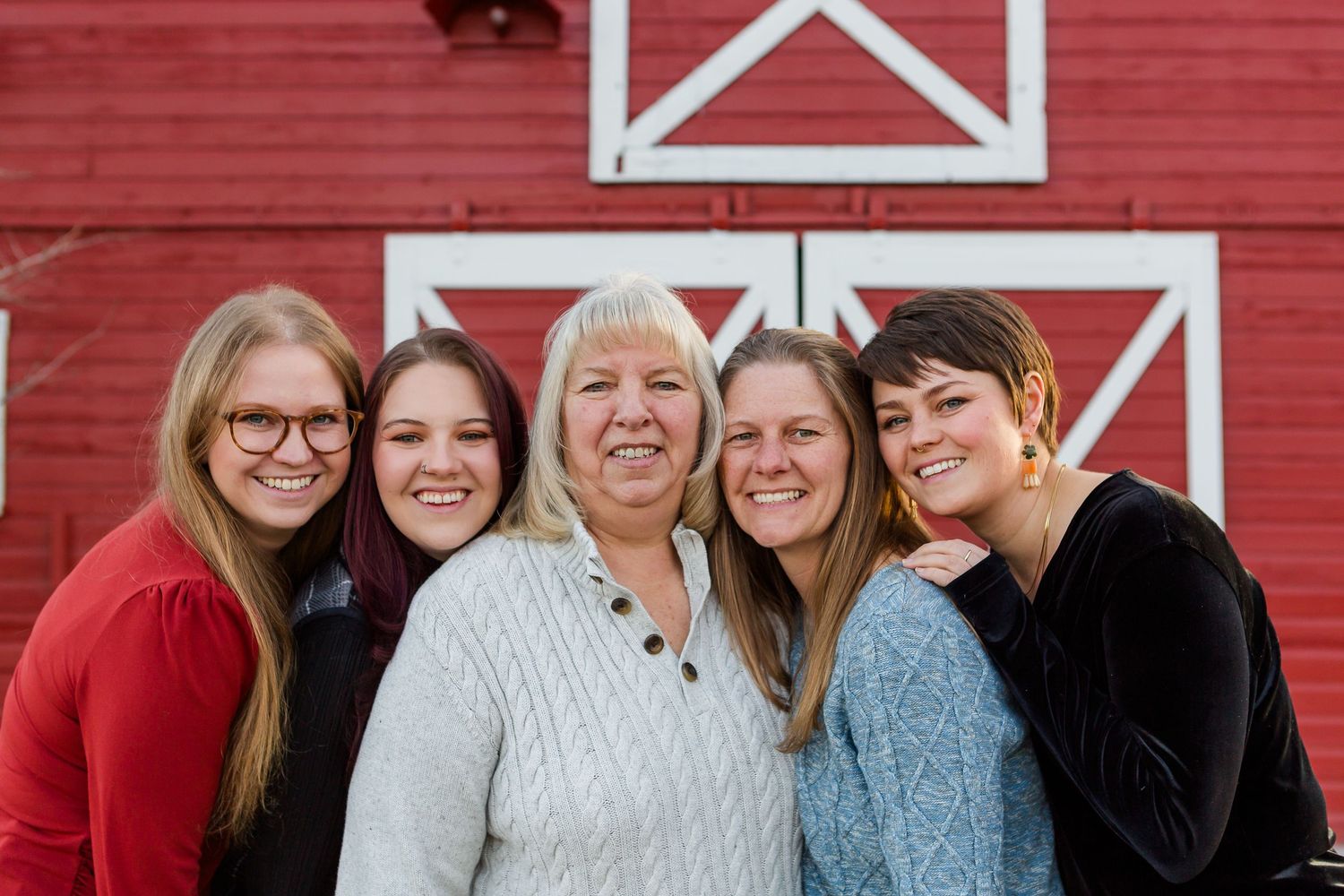 Five people smile warmly while posing together in front of a red barn with white X patterns.