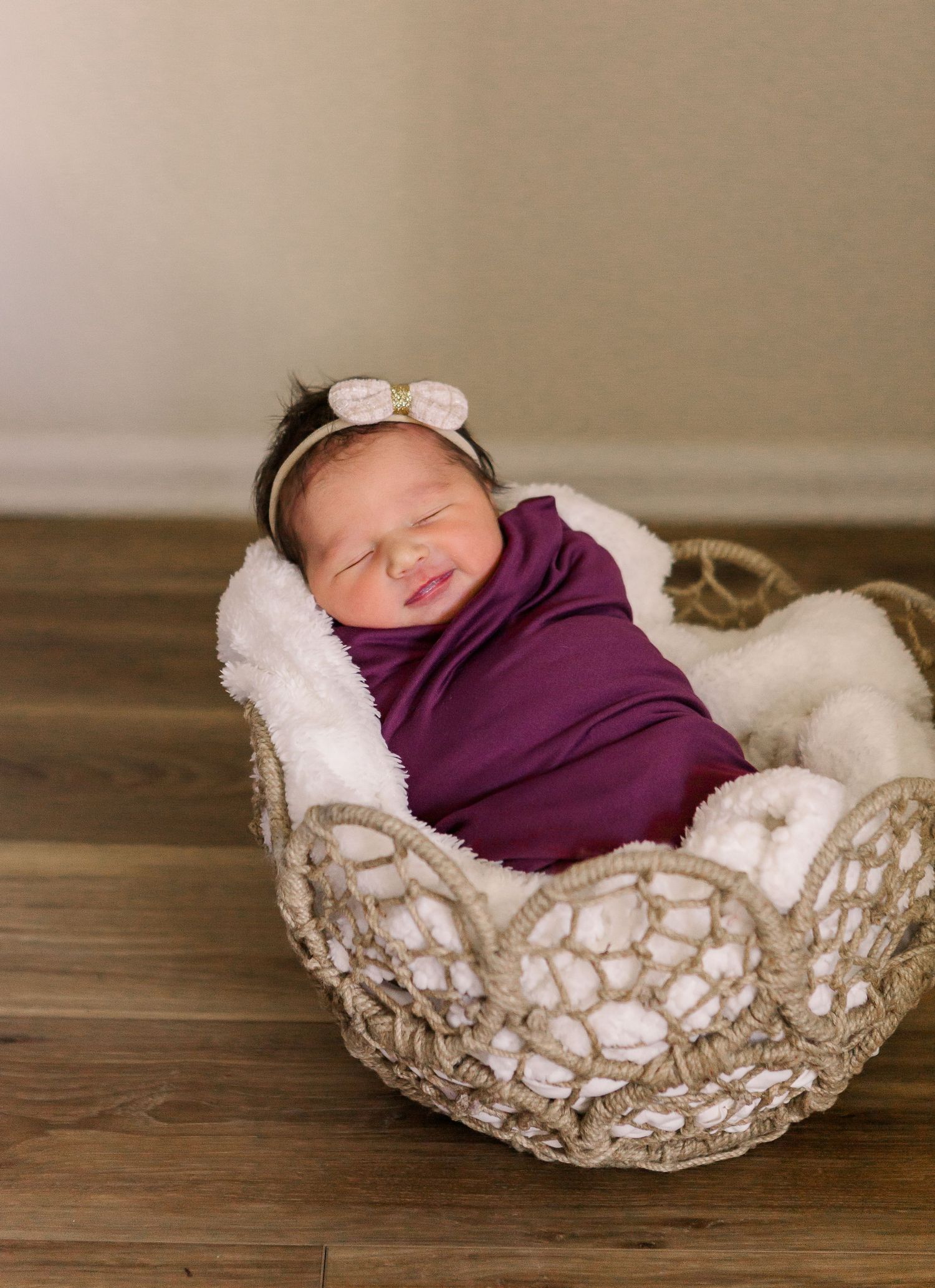 Smiling newborn in purple wrap sleeping in lace basket.