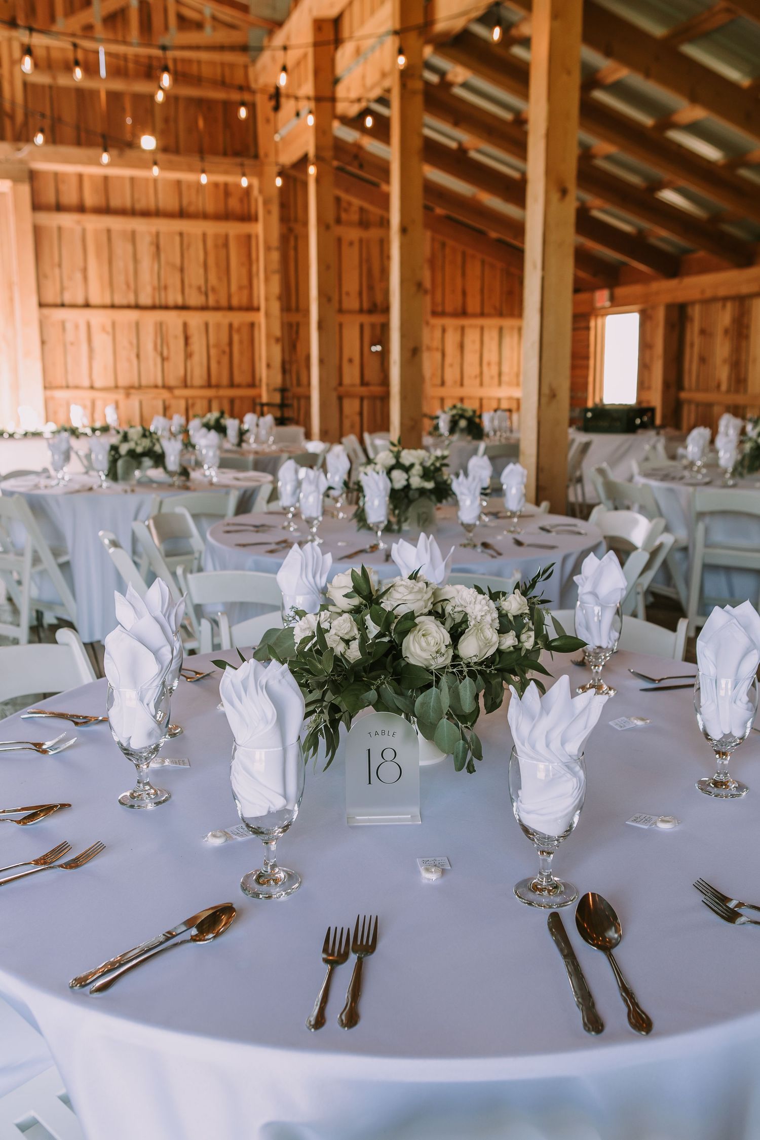 Rustic barn wedding reception with white table settings and floral centerpieces.