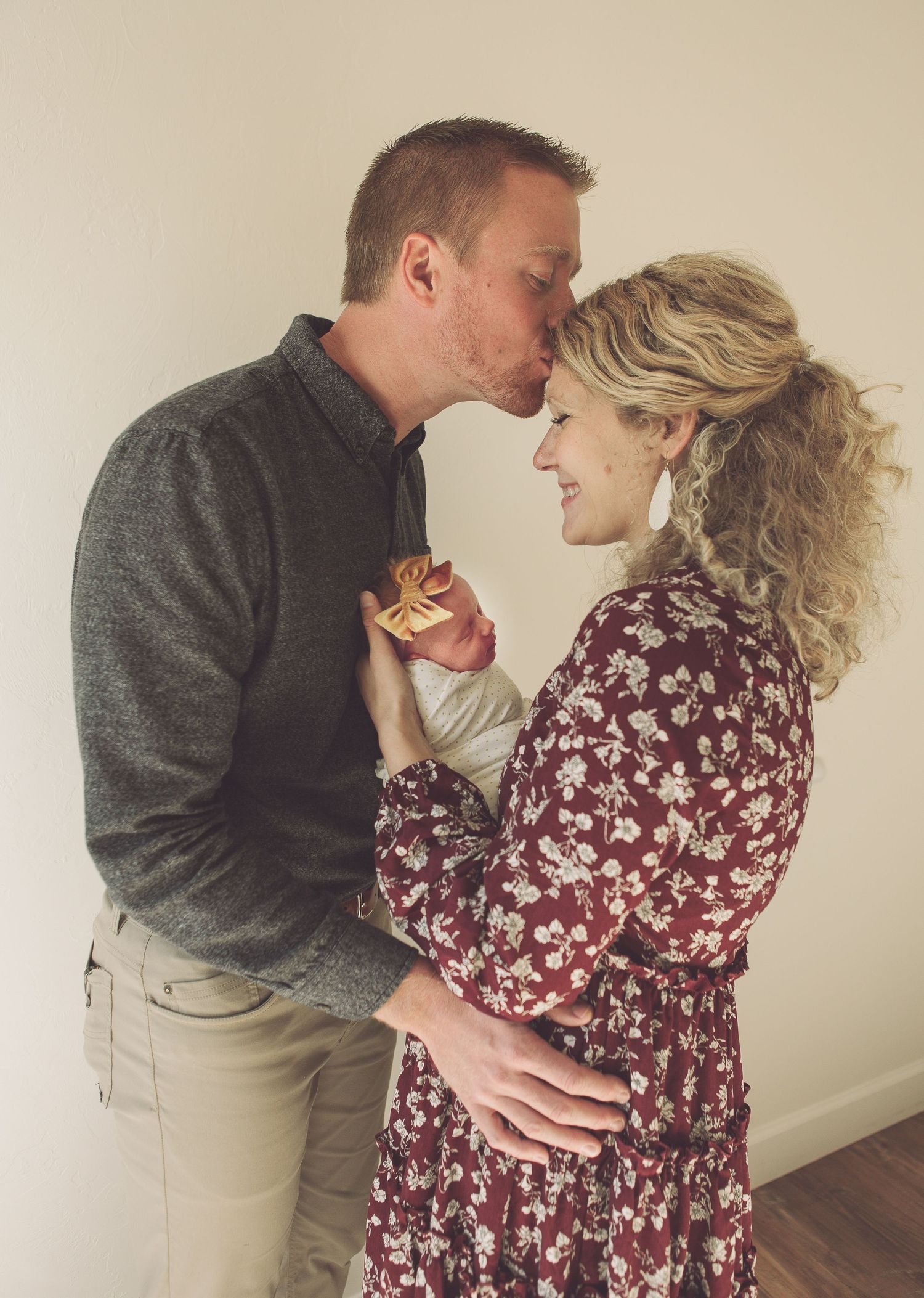 Romantic portrait of couple in grey sweater and burgundy dress holding their baby.