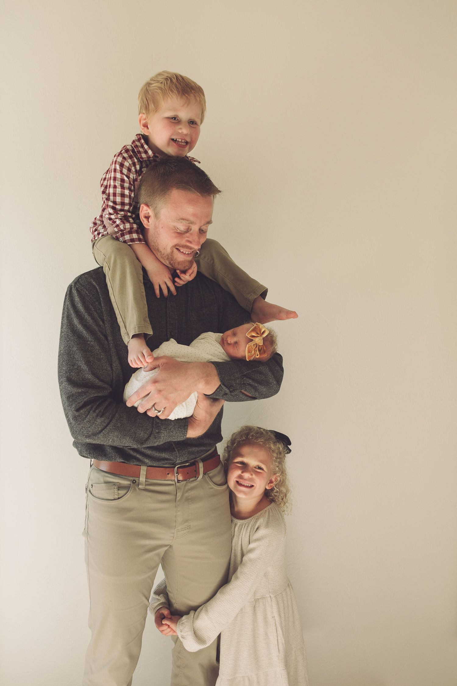 Joyful family photo with children climbing and hugging their father who holds a baby.