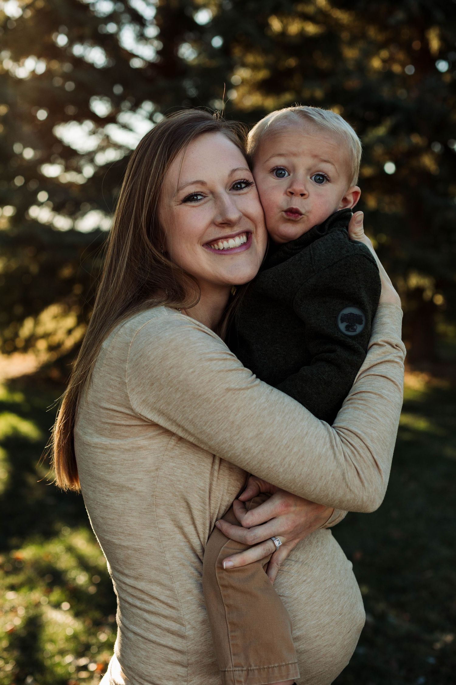 Mother and toddler share tender moment during maternity photo session with golden sunlight.