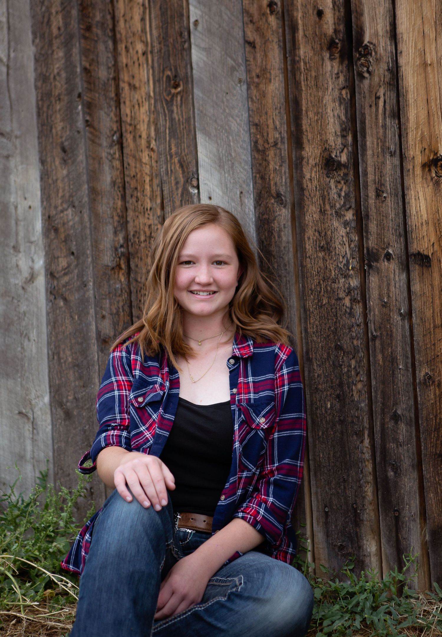 Portrait of person in plaid shirt sitting against rustic wooden wall.