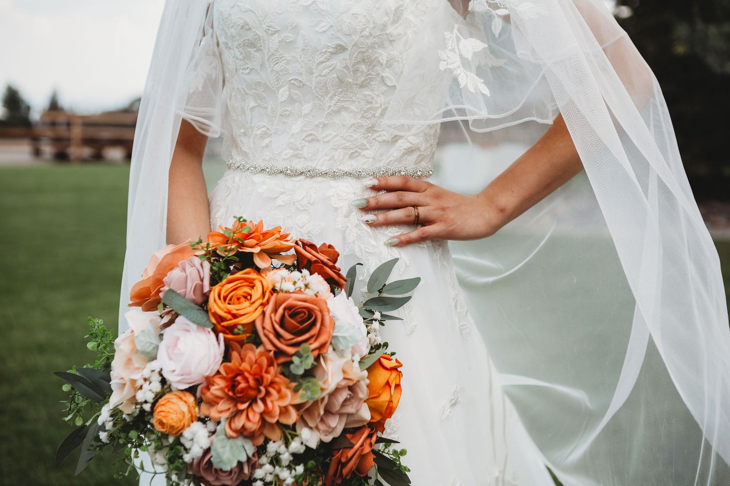Close-up of bridal bouquet with orange roses and white dress details.