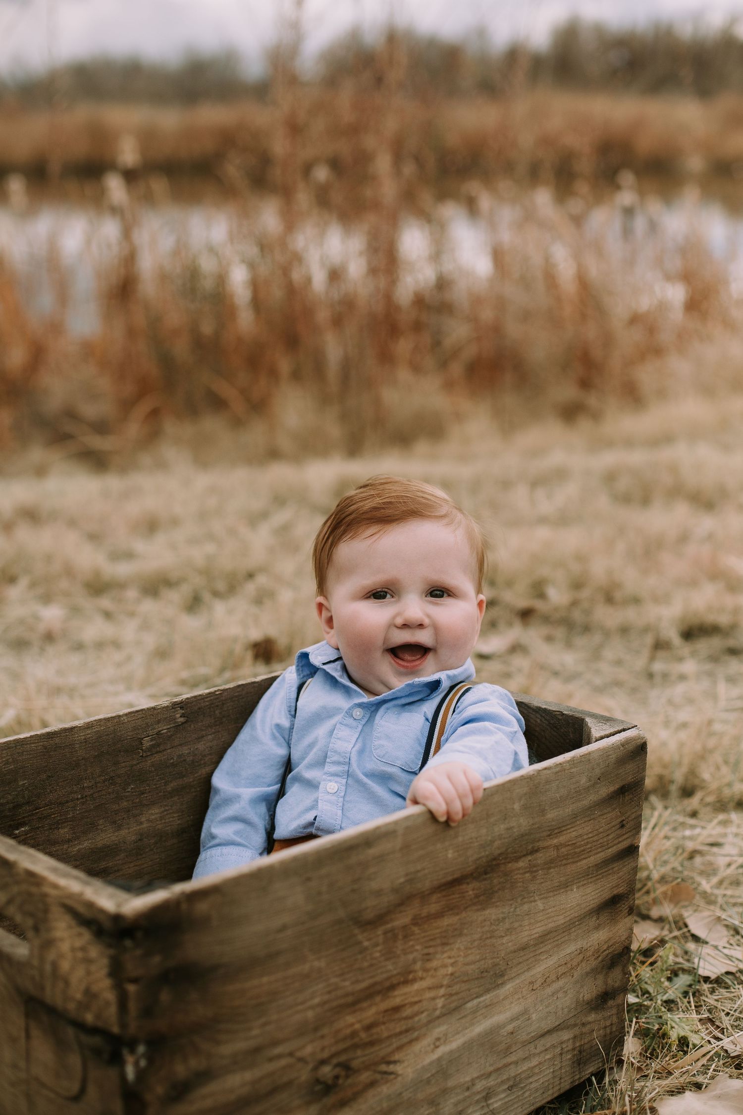 A happy baby sitting in wooden crate outdoors during golden hour.