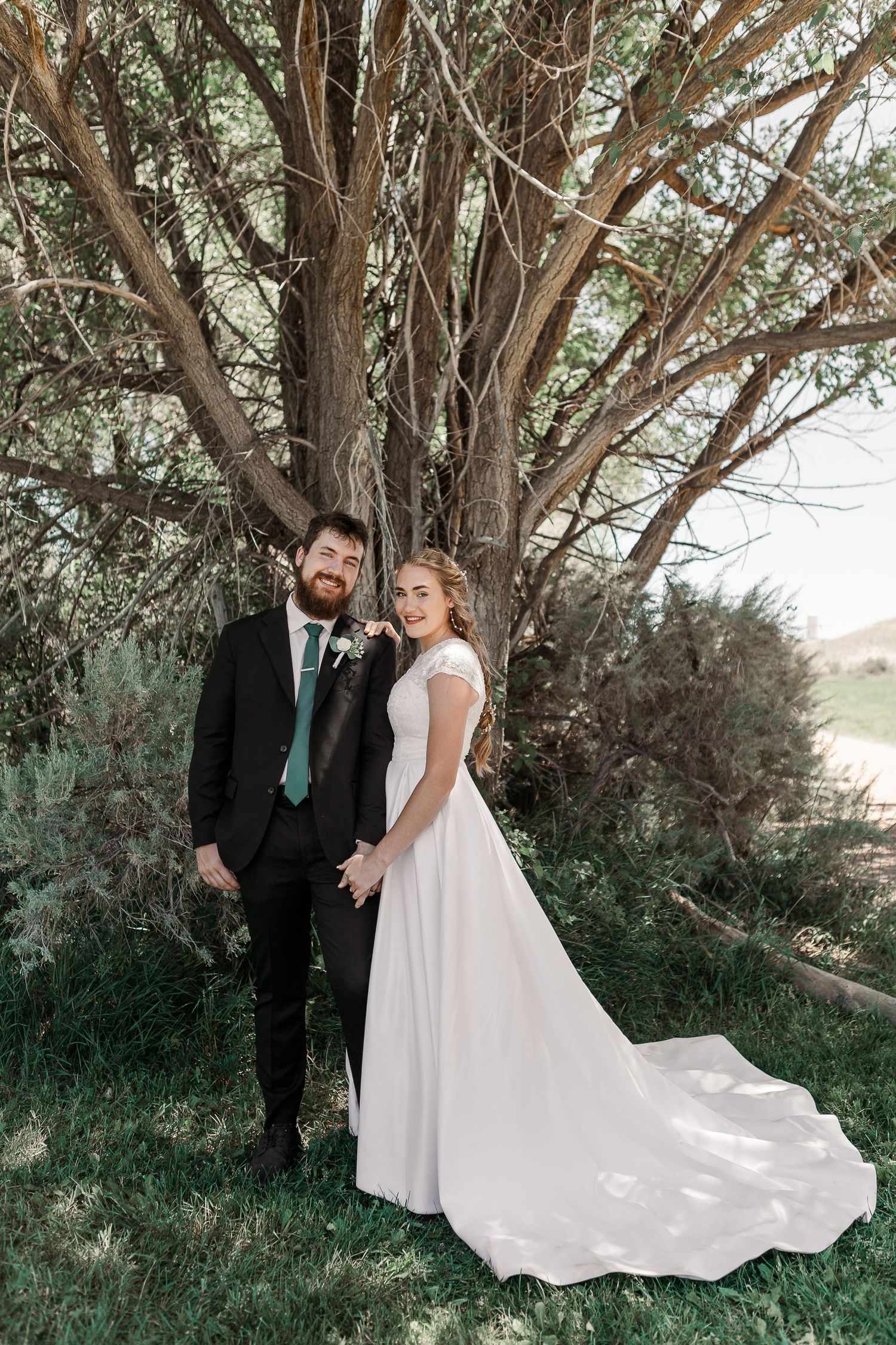 An elegant wedding portrait under a majestic tree with flowing white dress details.