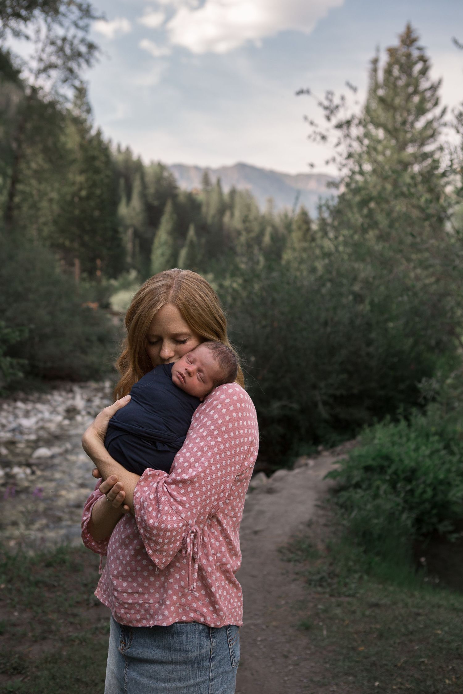Tender moment shared with infant along forested mountain path beside flowing stream.