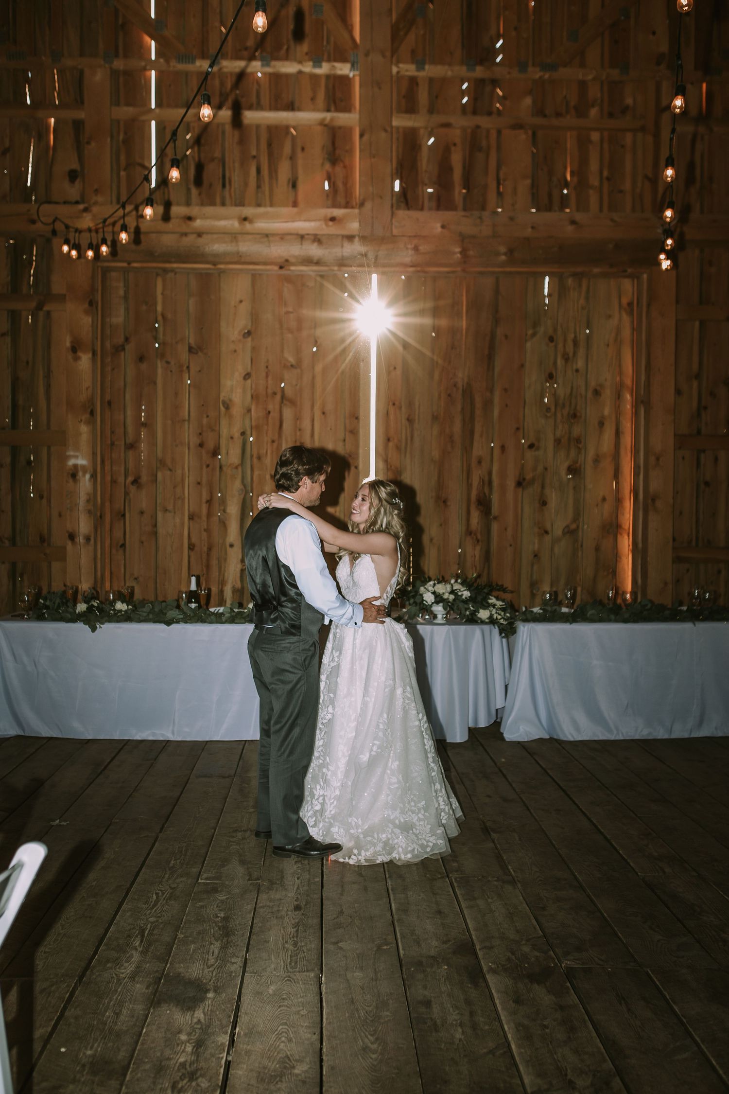 A romantic first dance in a rustic barn venue with twinkling lights and dramatic lighting.