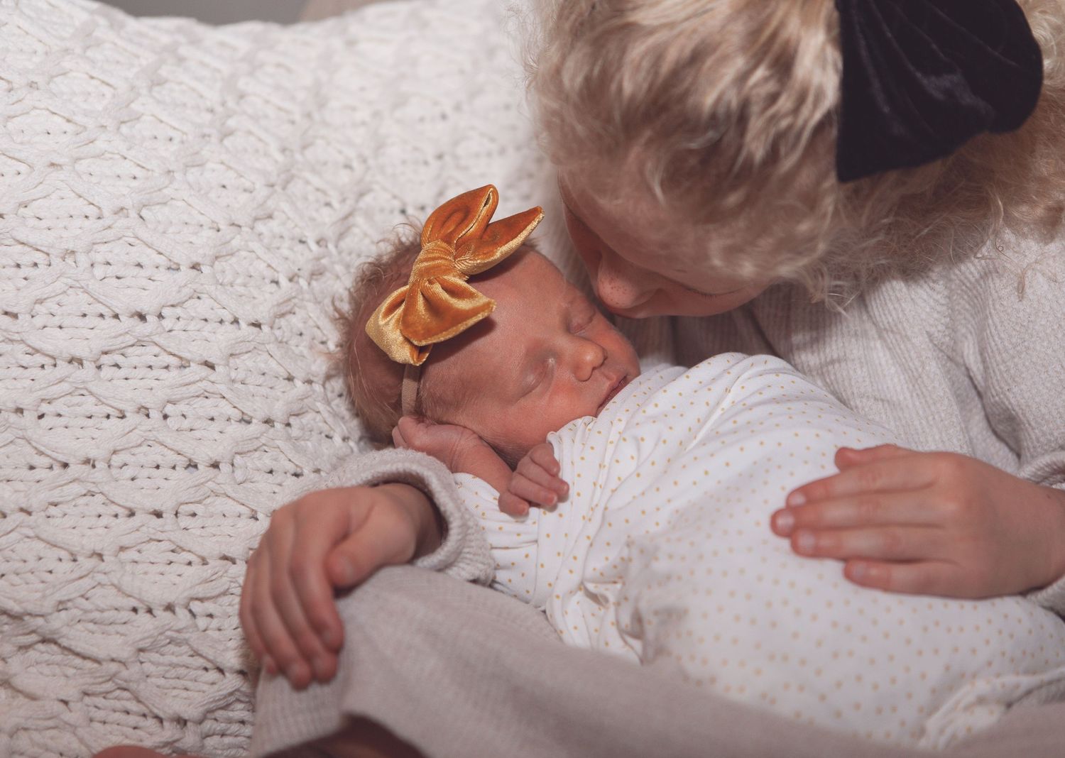 A sleeping infant wearing a golden crown lays on textured white bedding.