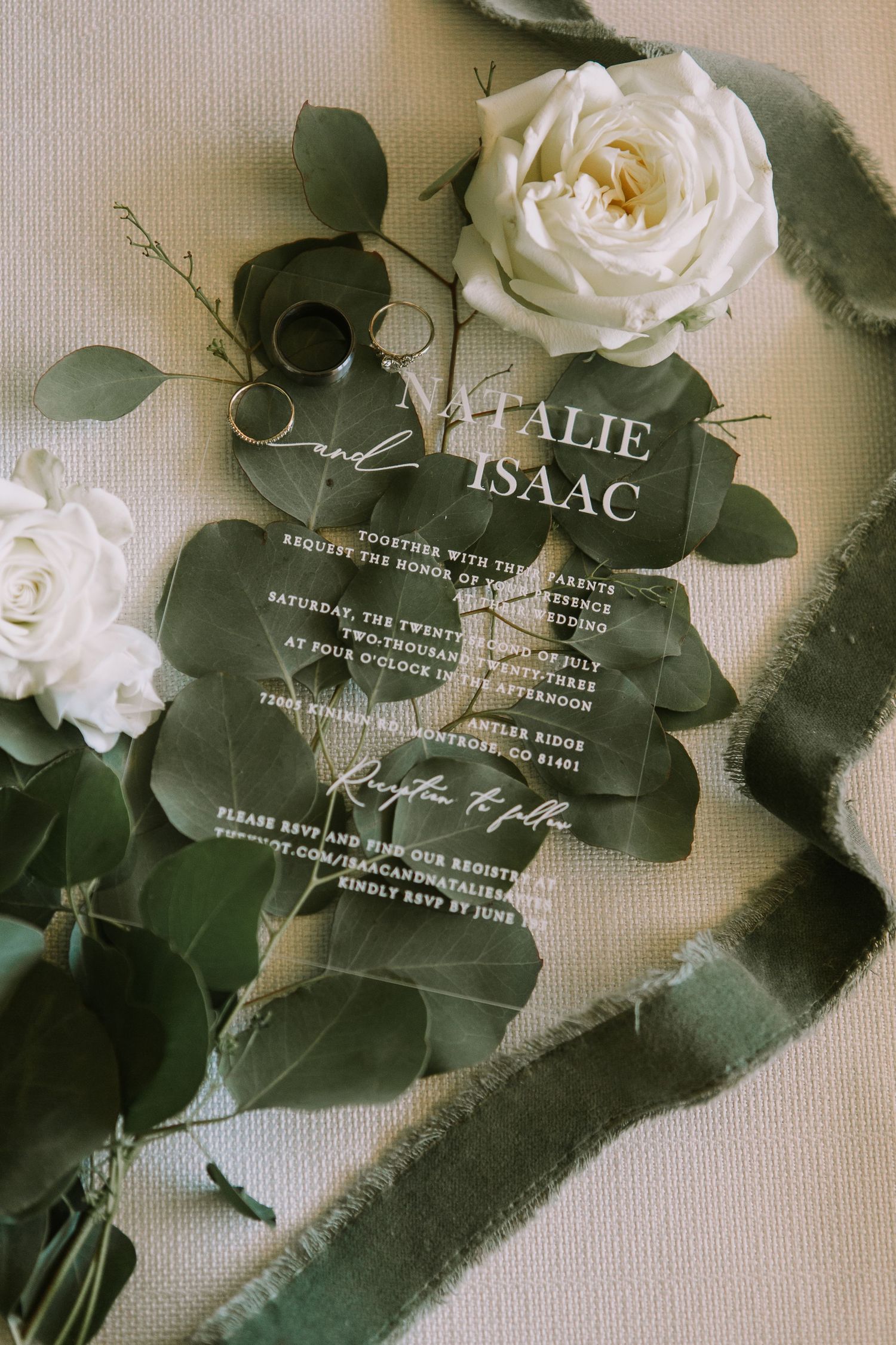 Clear wedding invitation surrounded by white roses and green foliage.