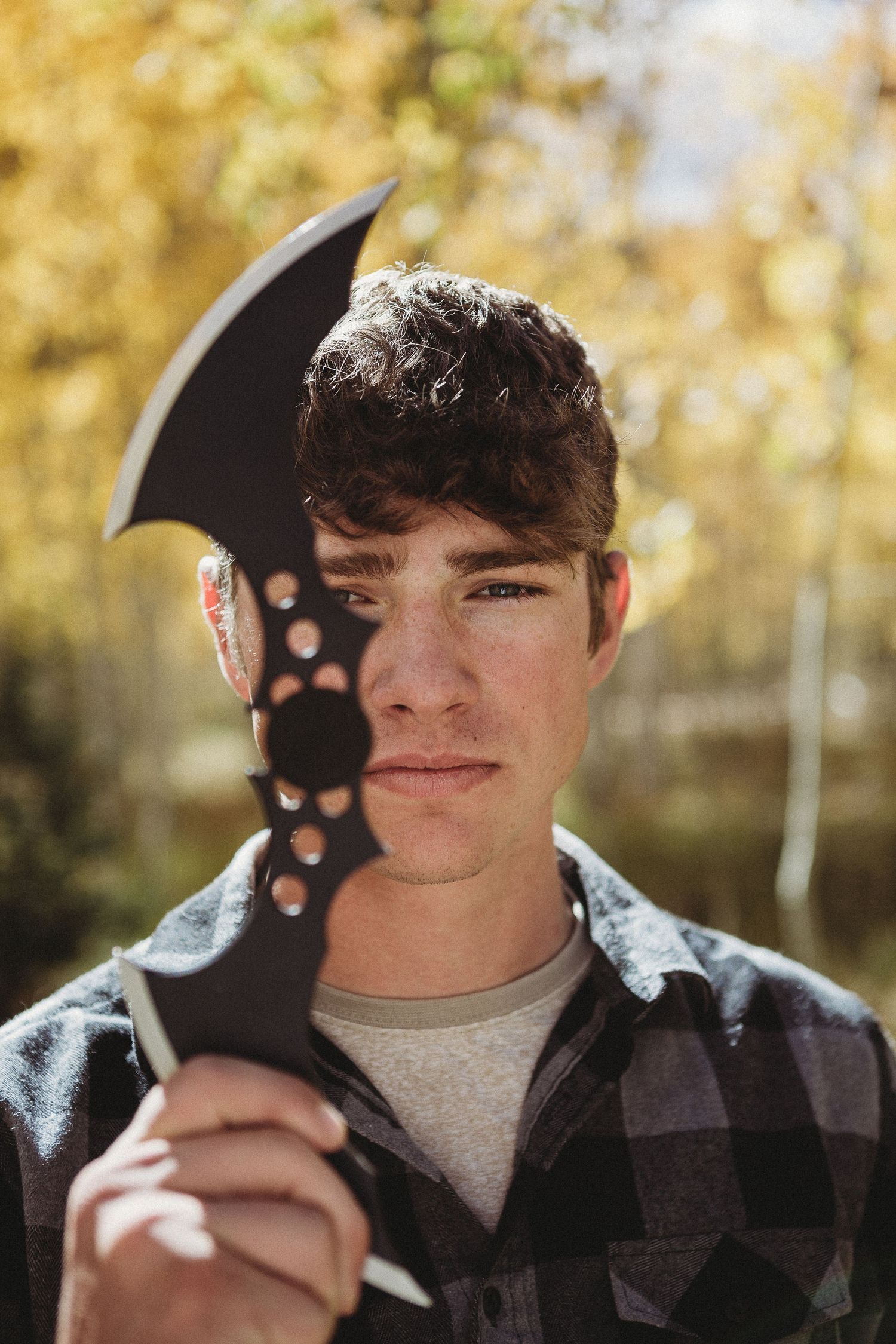 Person holding axe prop against autumn forest backdrop during portrait session.