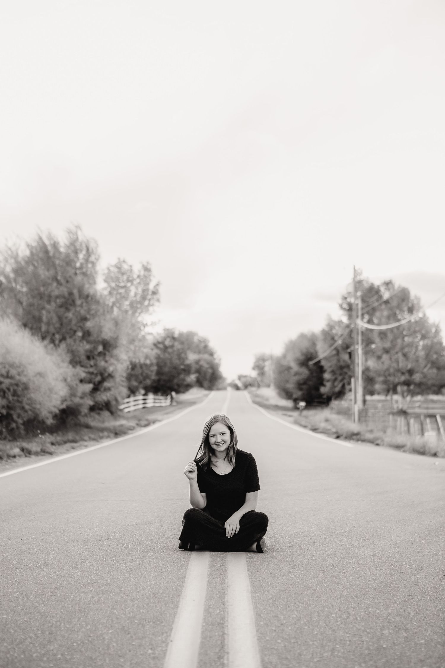 Black and white portrait of person sitting in middle of empty rural road.
