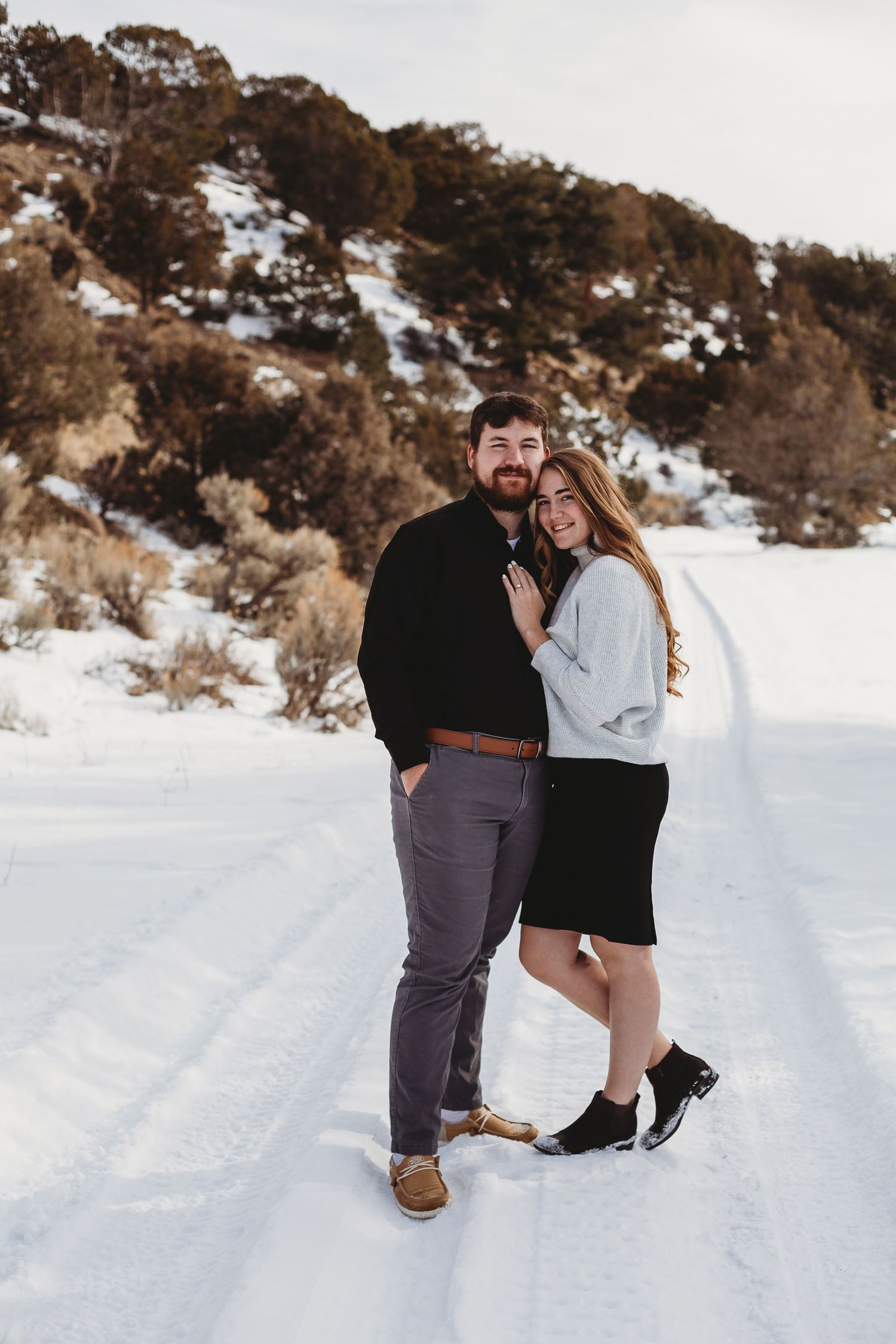 A romantic winter photoshoot of a couple embracing on a snowy mountain path.