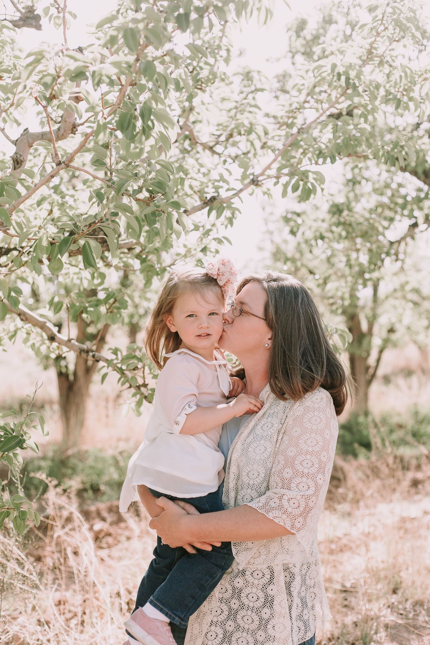 Sweet outdoor moment captured beneath blooming tree branches in soft lighting.