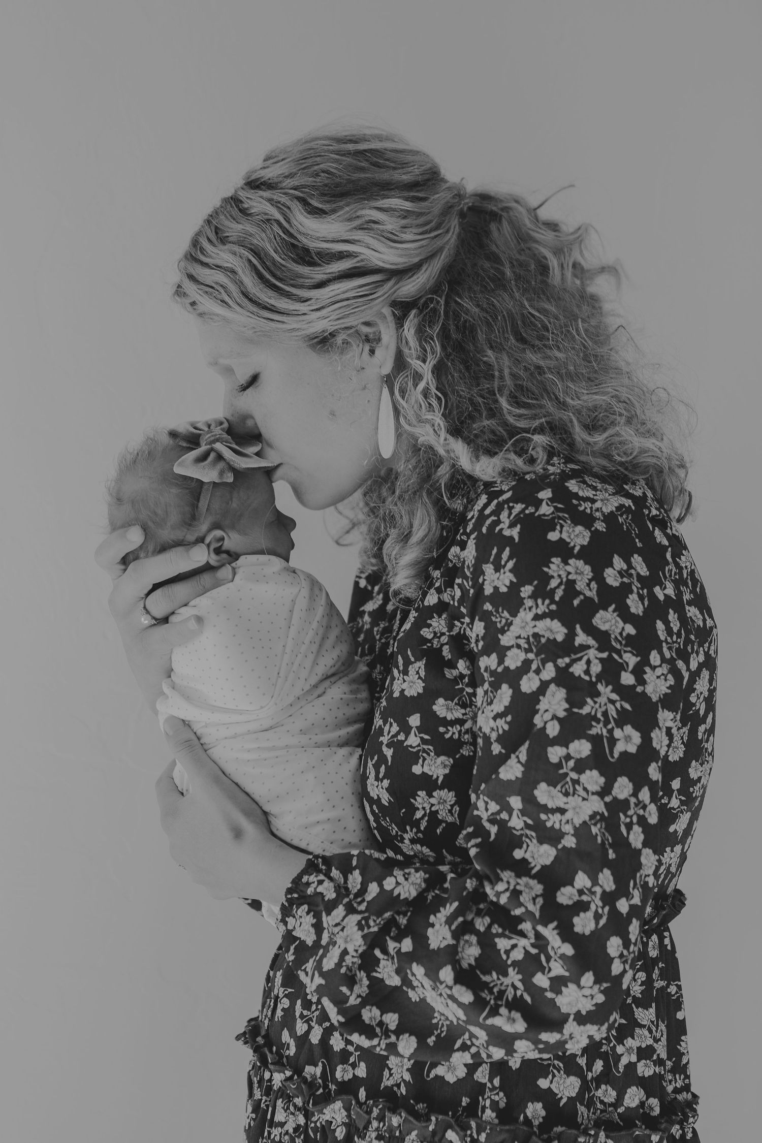 Black and white portrait of woman in floral dress holding swaddled baby.