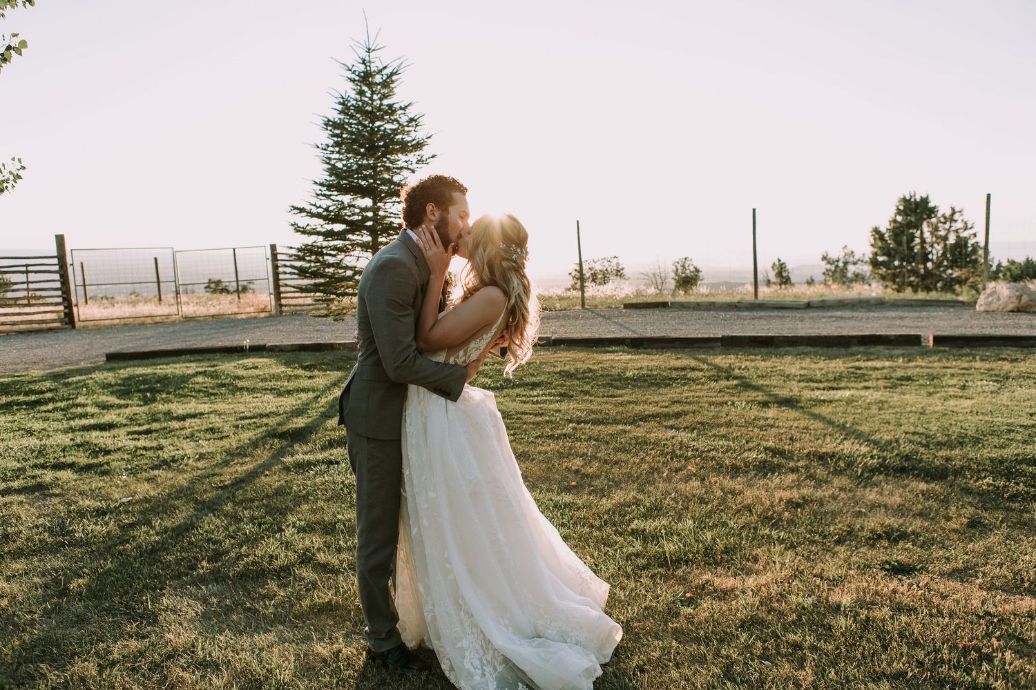 Golden hour wedding photo captures romantic moment between newlyweds on grassy lawn.