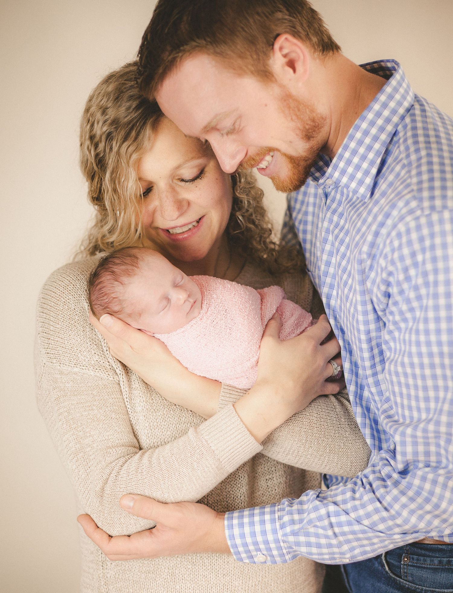 Intimate portrait of parents sharing a tender moment with their sleeping newborn in natural light.