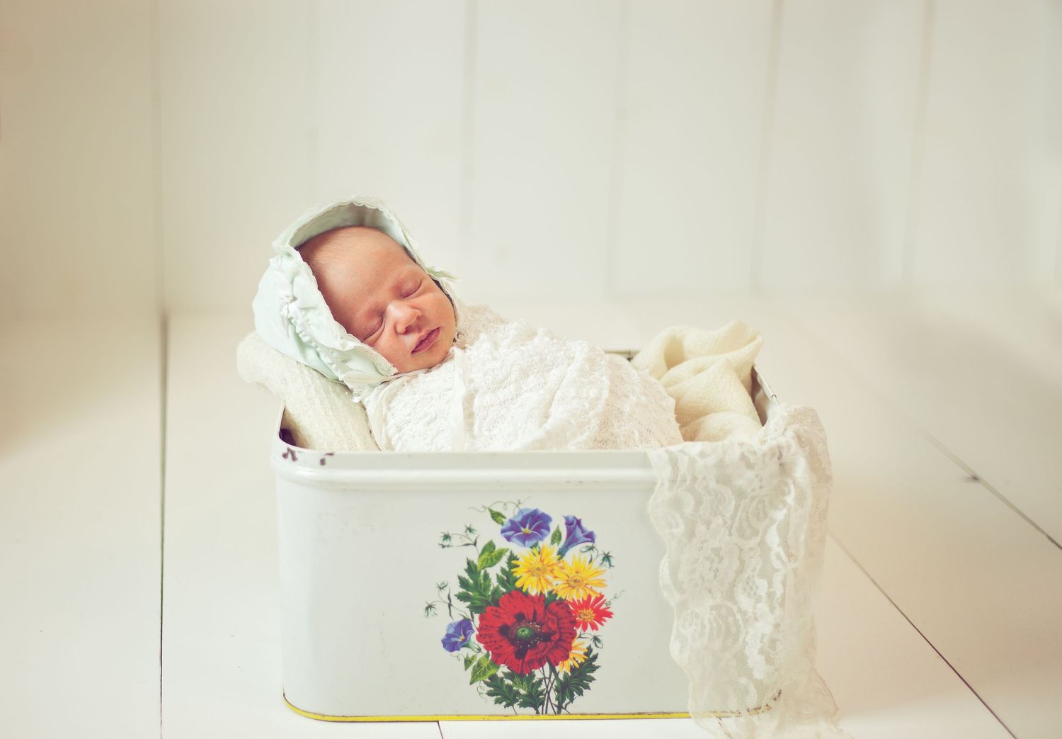Sleeping newborn lying in vintage white tin container with floral decoration.