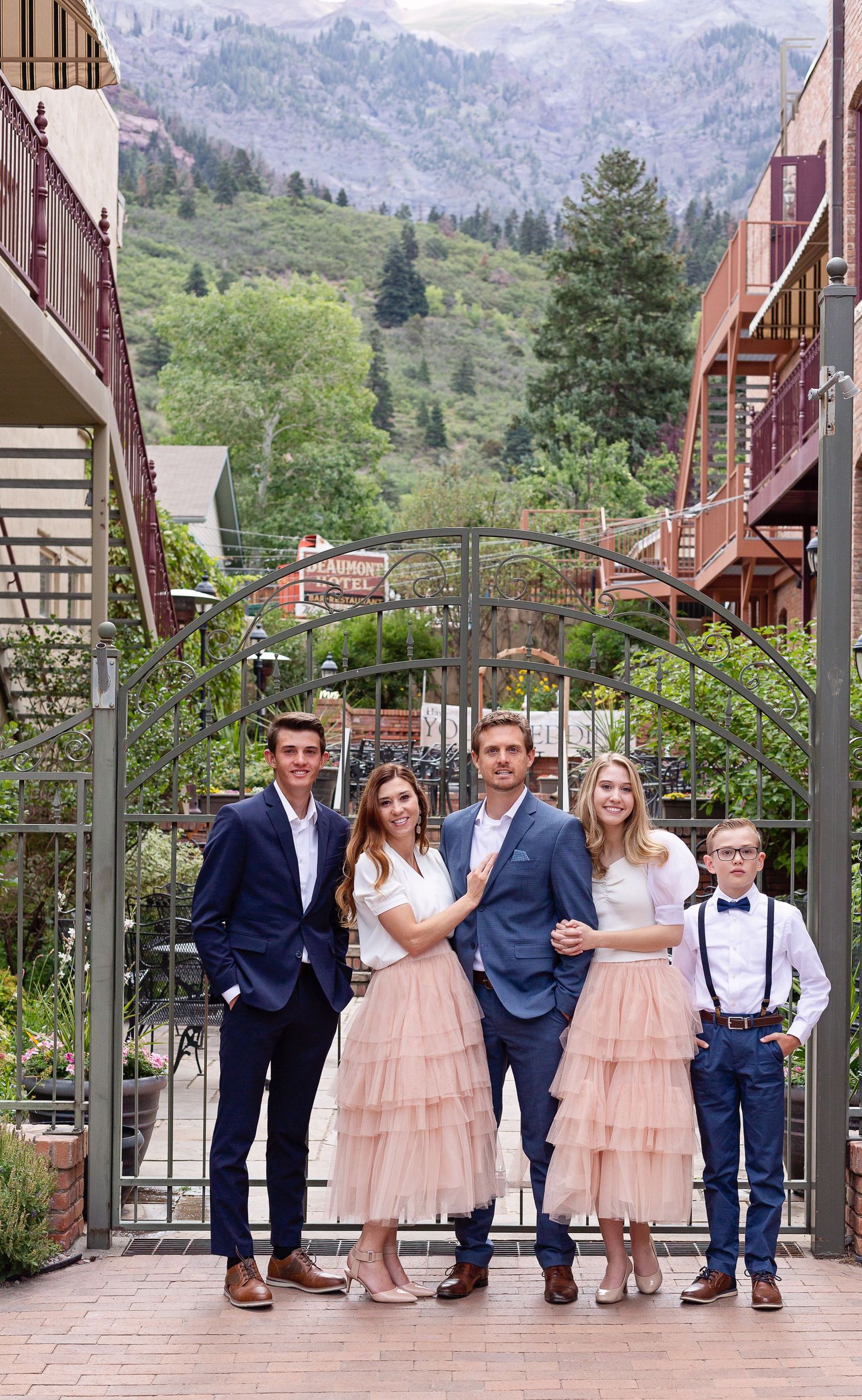 Wedding party poses in front of mountain scenery with rustic buildings and evergreen trees.
