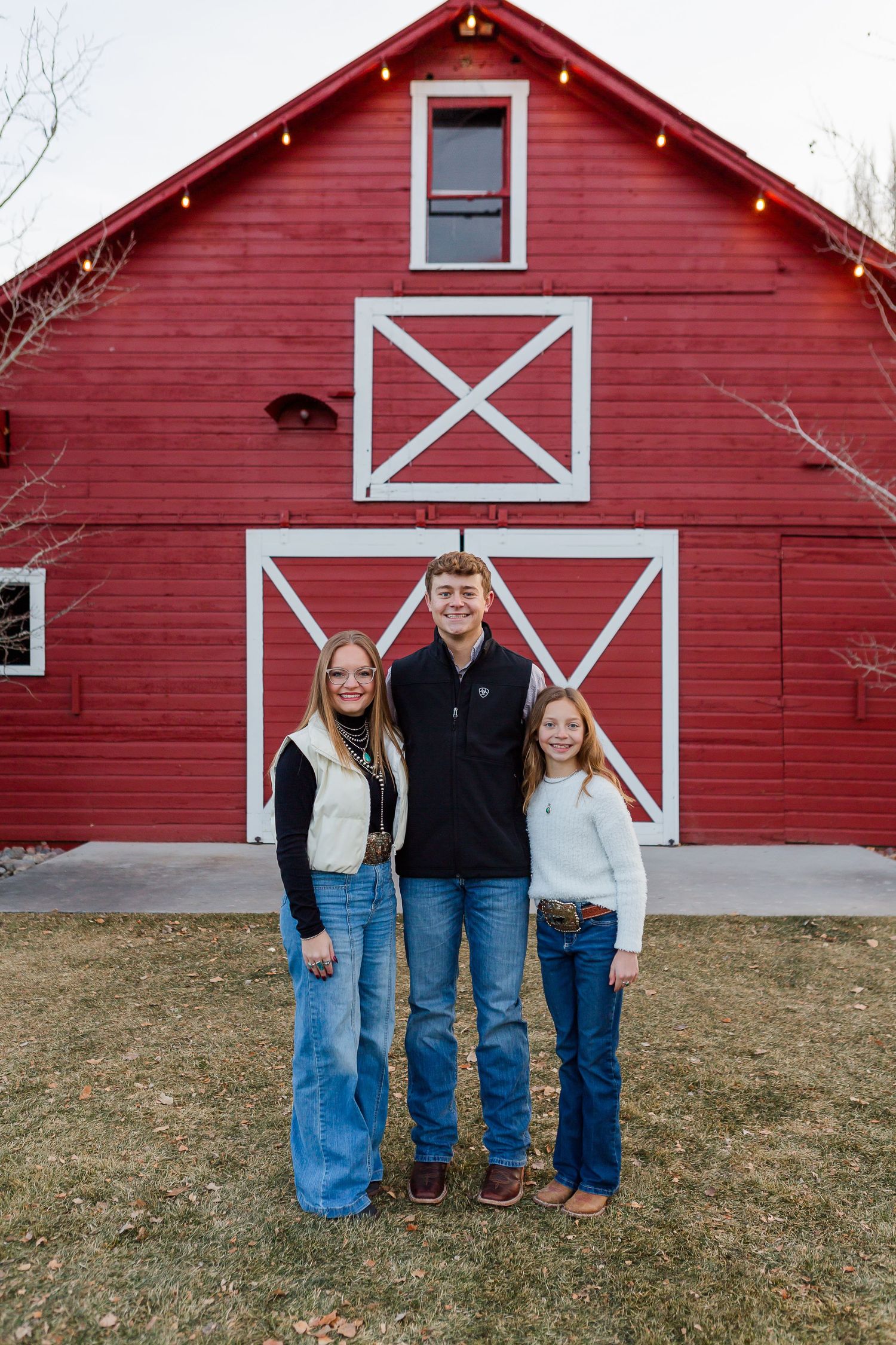 A small group poses together in front of a red barn with white trim and decorative lighting.