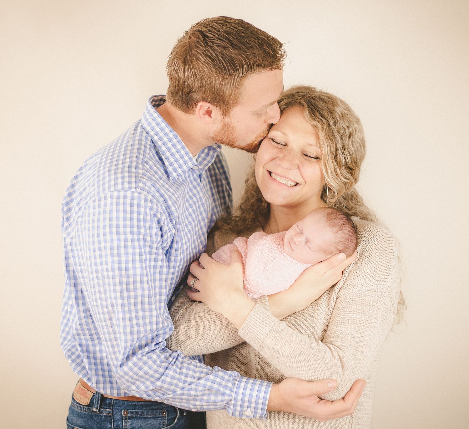 Tender family moment as parents share an intimate embrace while holding their sleeping newborn.