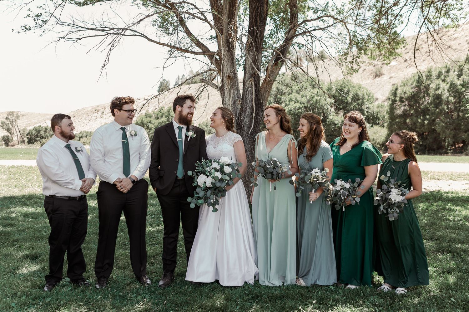 Wedding party group photo with bridesmaids in green dresses and groomsmen in dark suits.