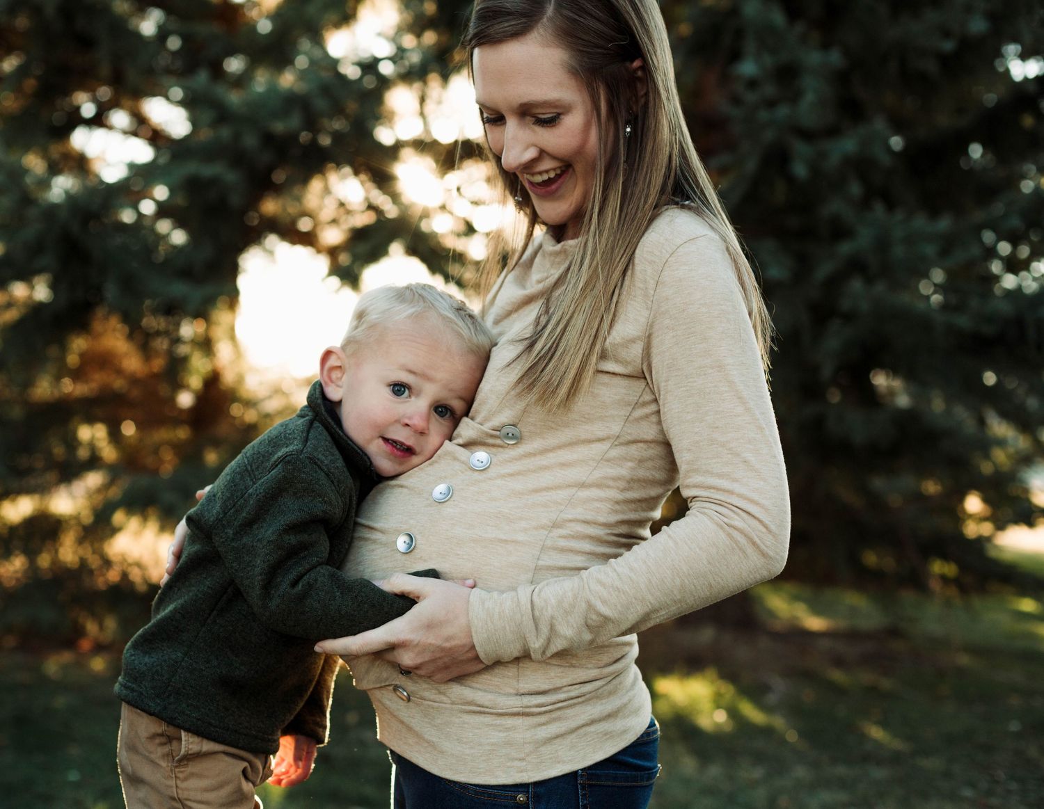 Outdoor maternity photo at sunset with evergreen trees in background.