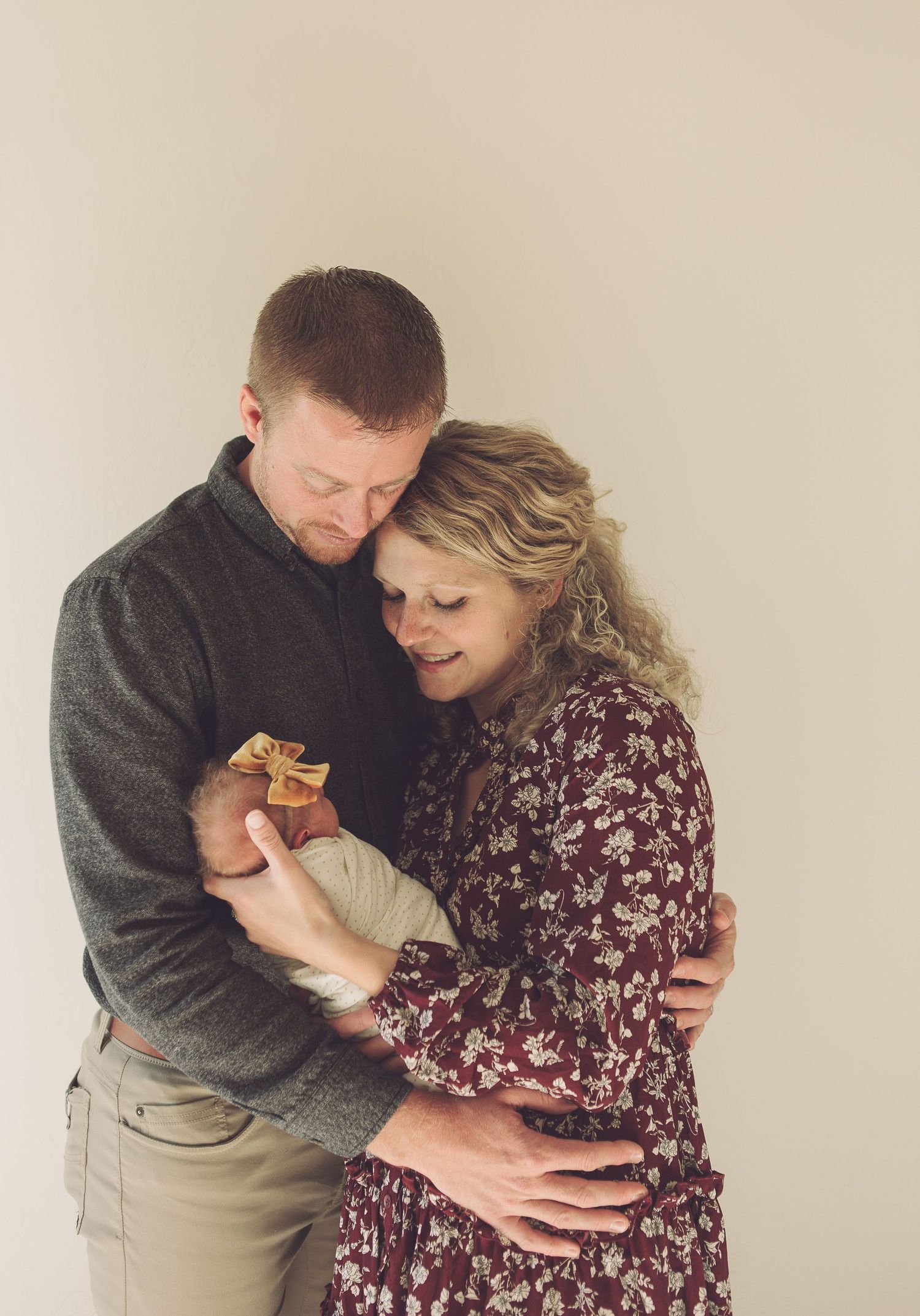 An intimate family portrait showing parents embracing while holding their newborn.