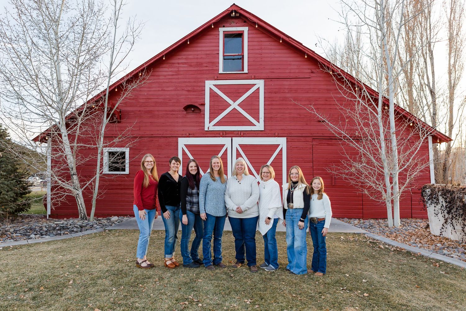 A group poses together in casual attire against a bright red barn with white trim on a winter day.