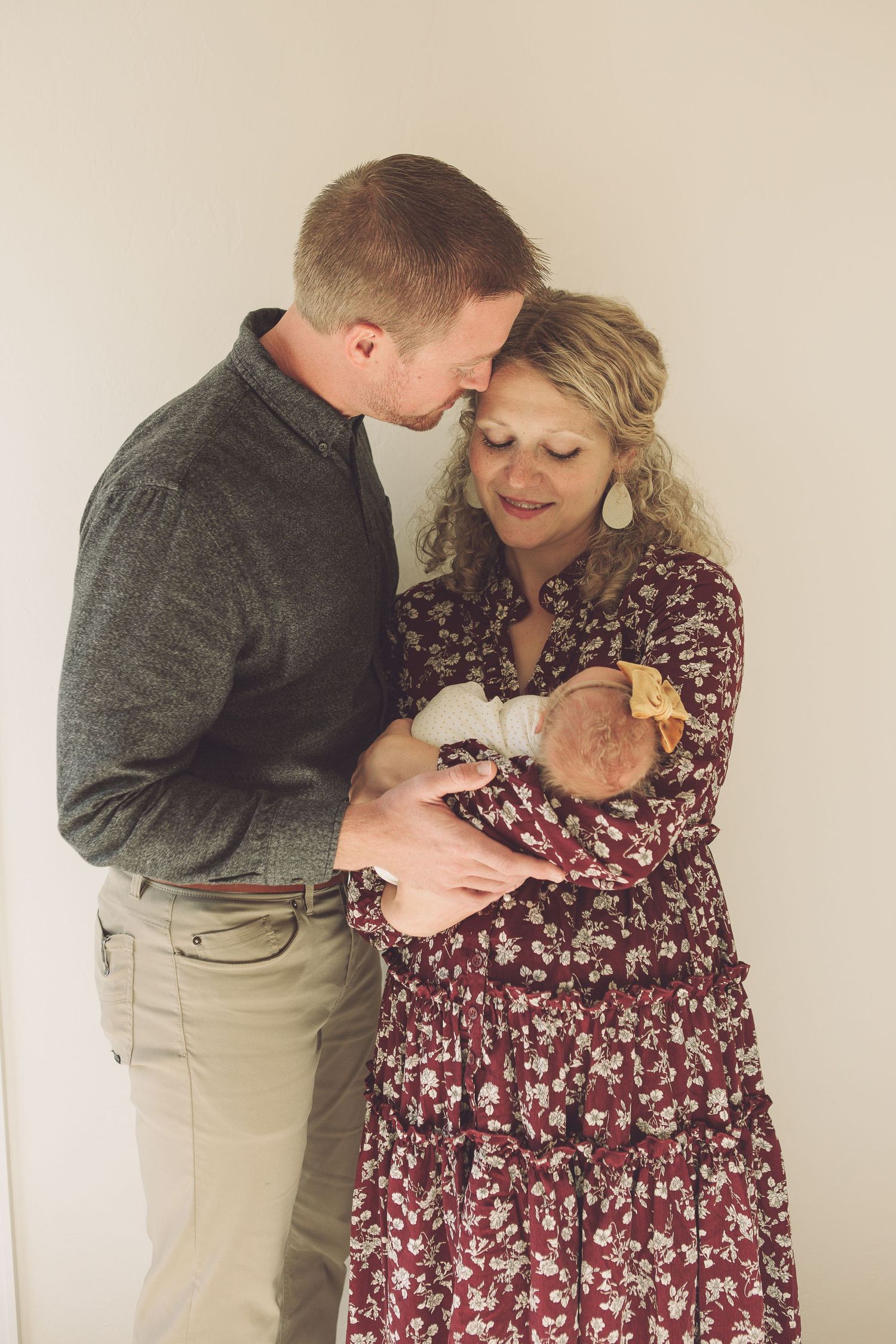 A tender family moment as parents cradle their newborn baby while wearing grey and floral burgundy outfits.