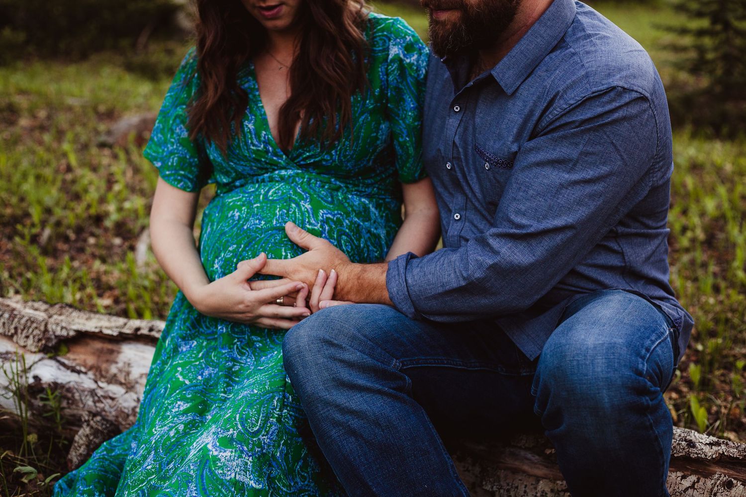 An intimate maternity portrait showing gentle hands cradling a pregnant belly in a forest setting.