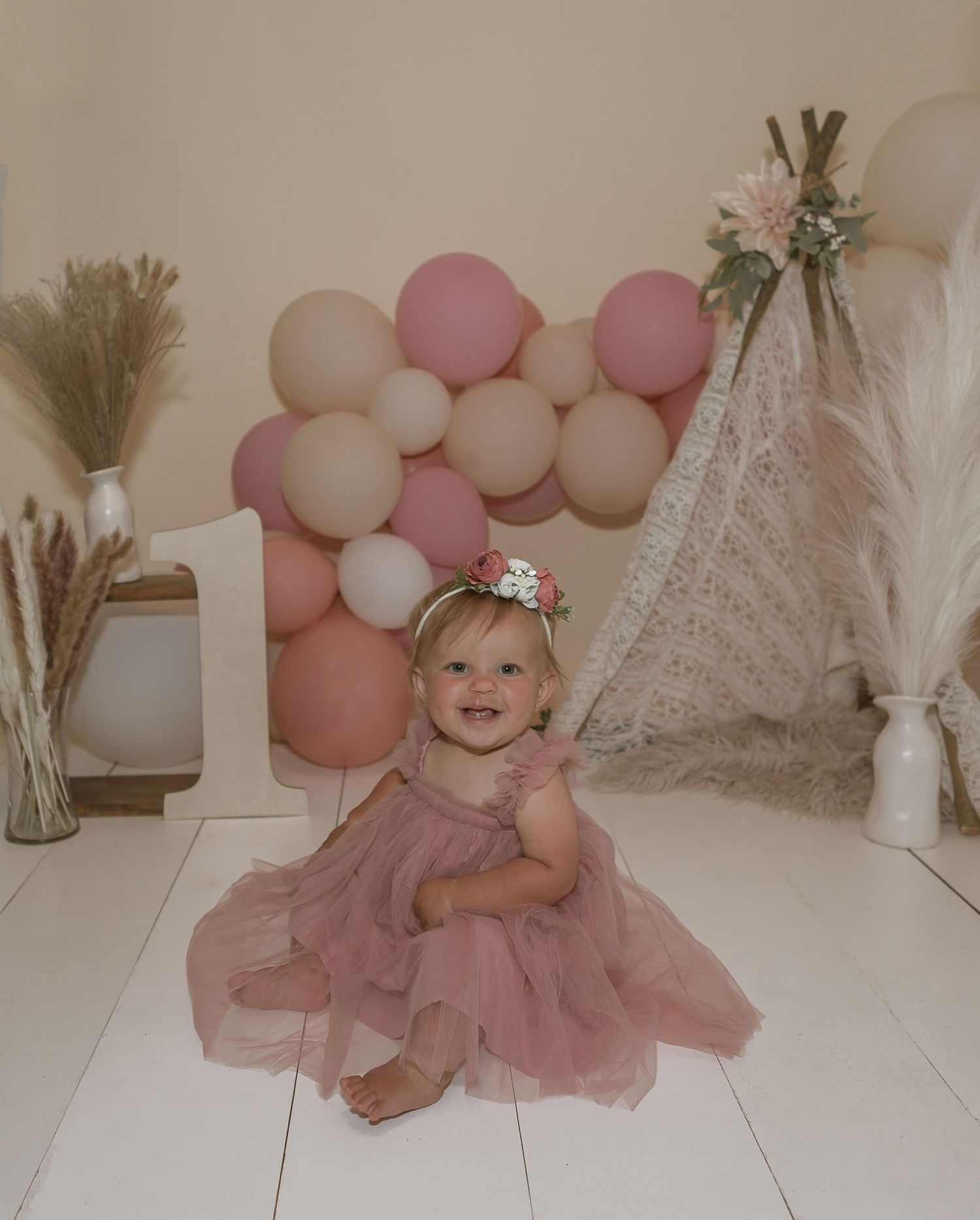 Baby in dusty rose tulle dress with balloon arch and boho teepee backdrop.