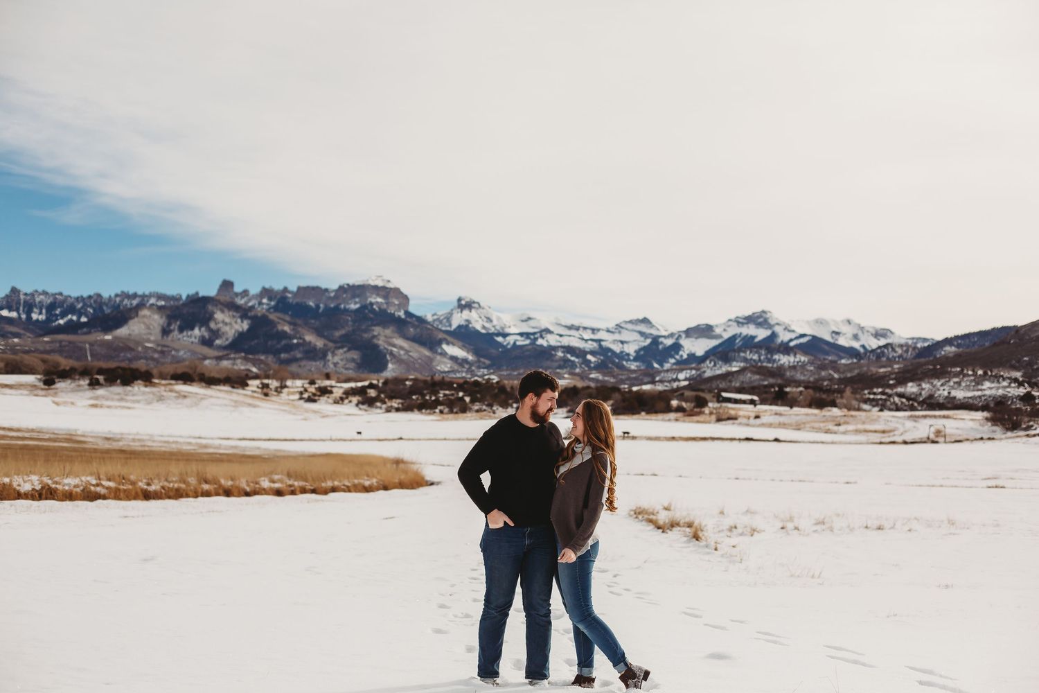 Winter engagement photo with snow-capped mountains creating dramatic background.