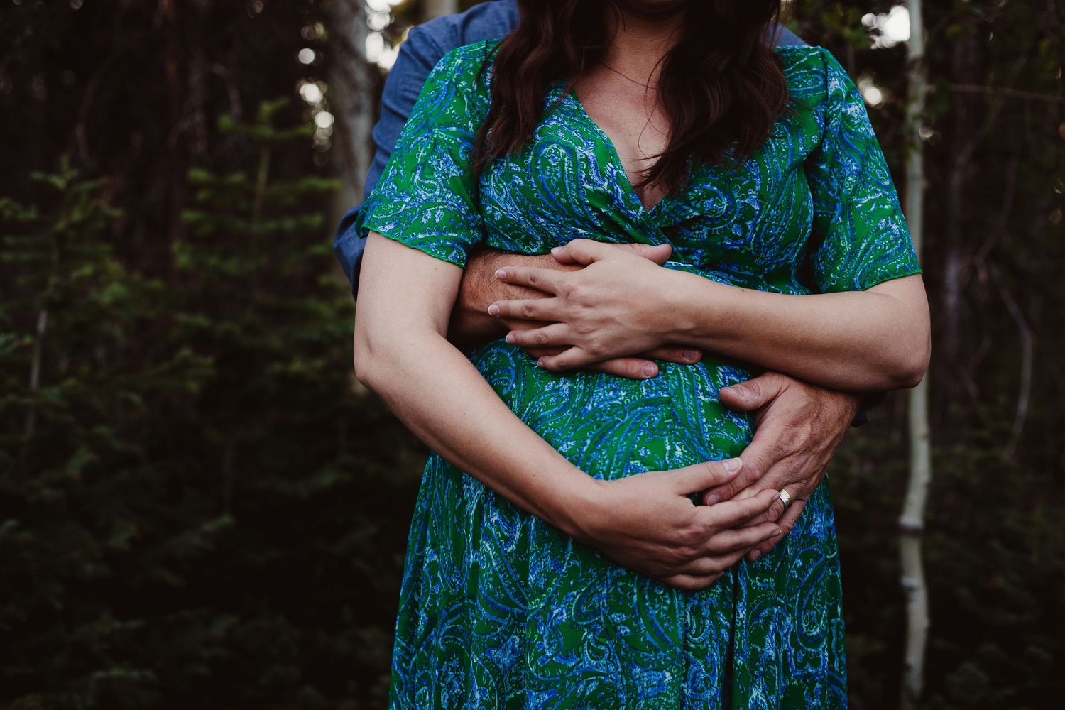 A close-up maternity shot showing gentle hands cradling a pregnant belly in a teal dress.