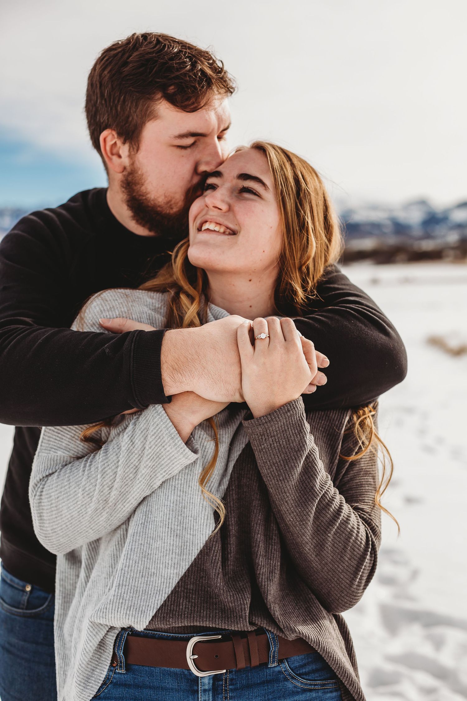 An intimate moment between a couple embracing in winter clothing against a mountainous backdrop.