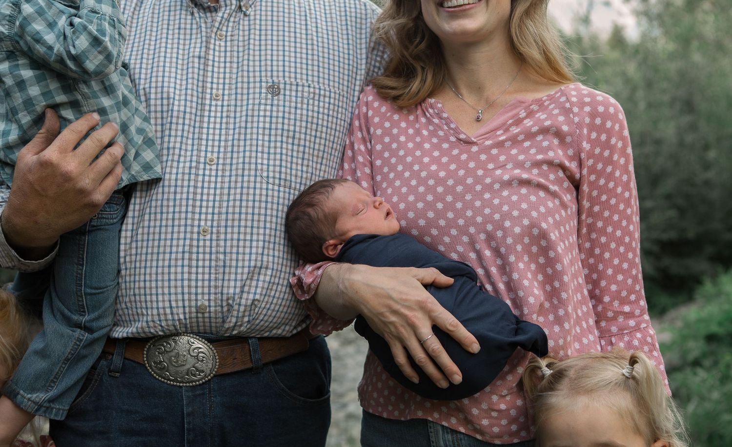 Casual family portrait showing parents holding their baby in outdoor setting.