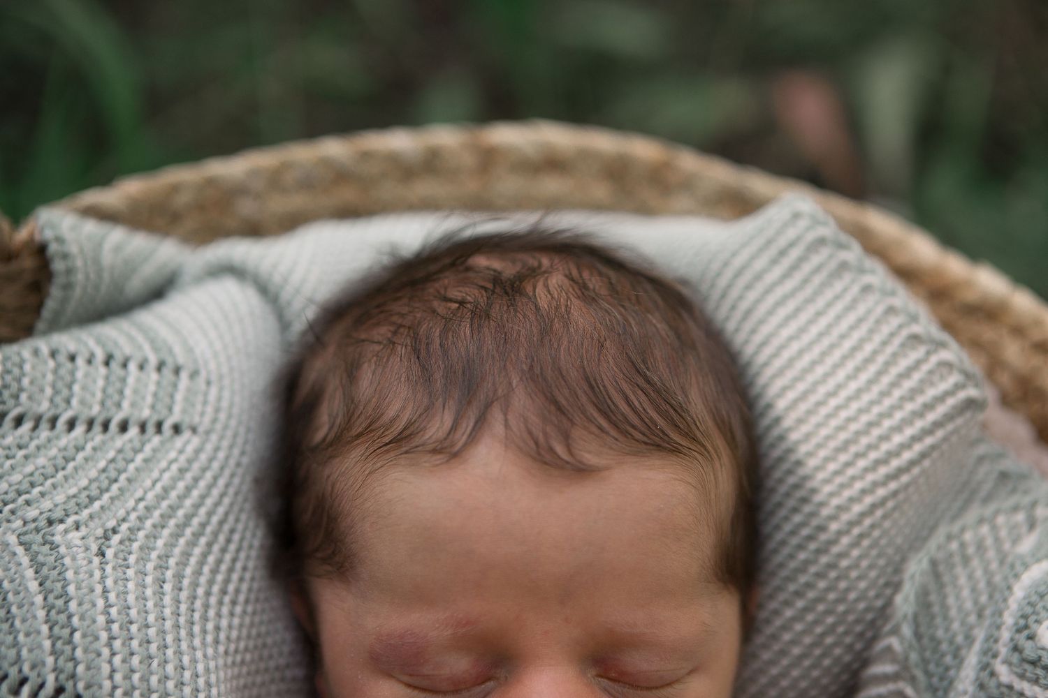 Close-up view of sleeping newborn wrapped in gray knit blanket in woven basket.