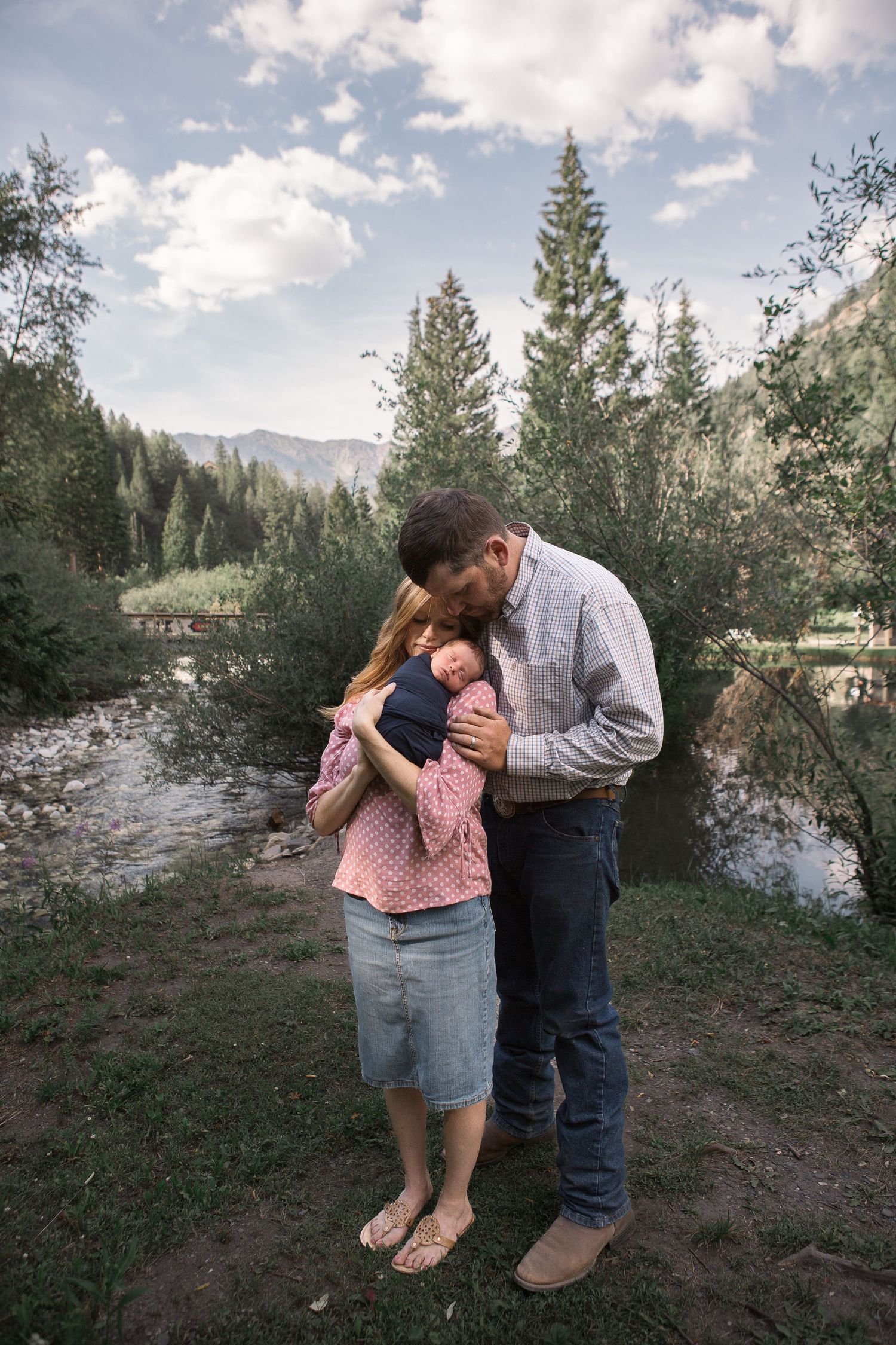 Intimate moment shared on forest trail with mountain stream and evergreens in background.