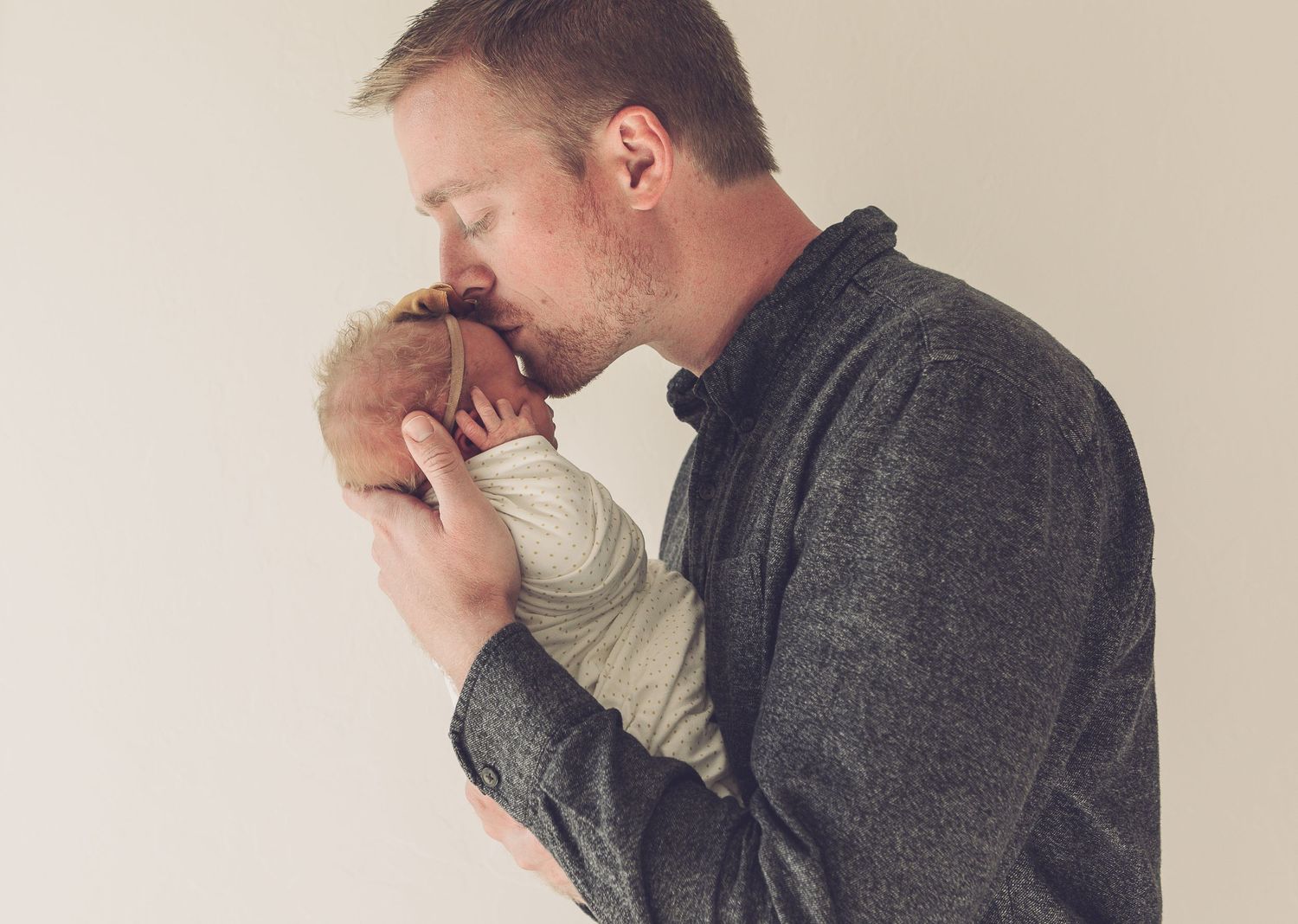 Intimate moment captured as parent in grey sweater kisses newborn baby's head.