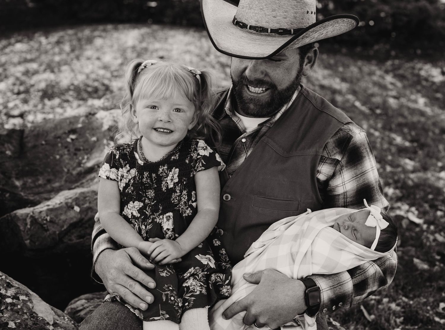 Family enjoying tender outdoor moment together on rustic bench in black and white photograph.