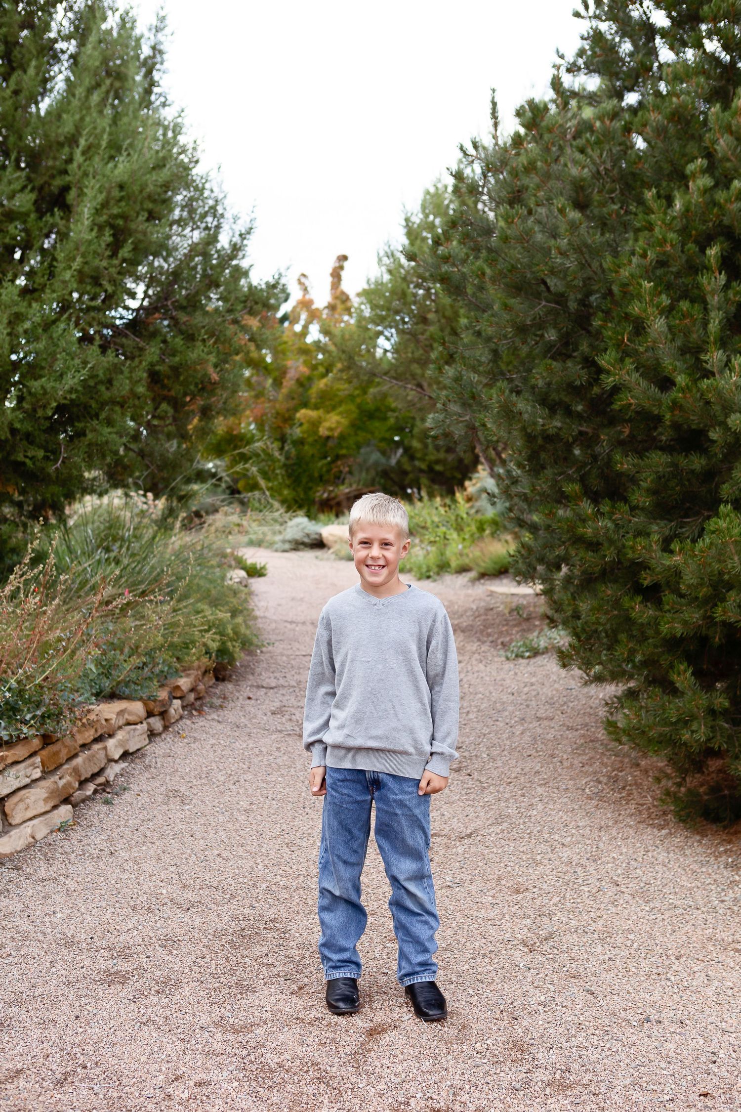 Casual figure standing on gravel path between evergreen trees in outdoor setting.