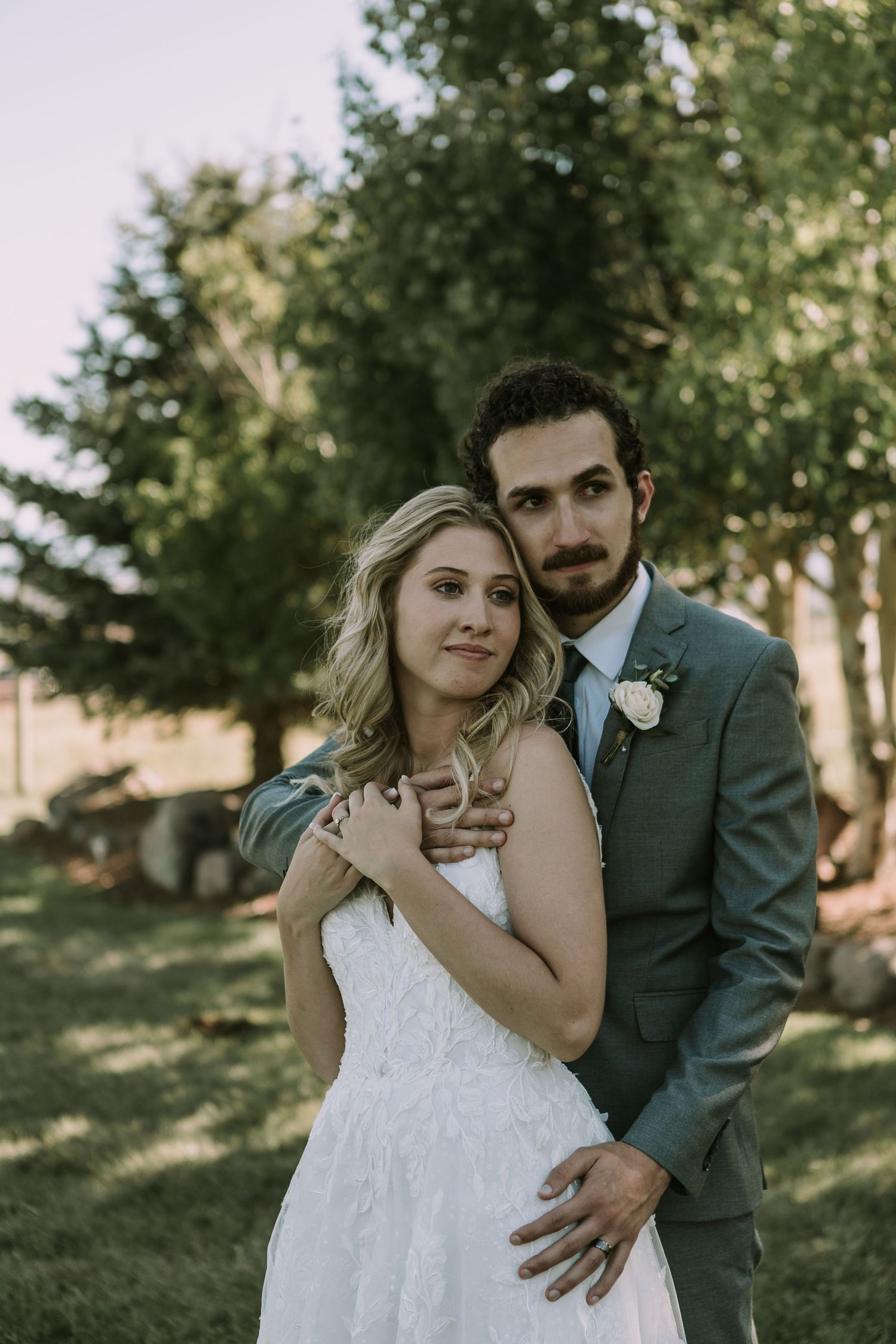 A tender wedding moment captured outdoors with natural lighting and greenery in the background.