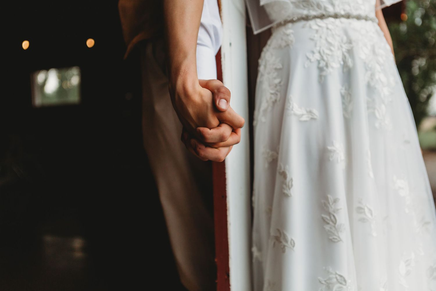 Close-up shot of couple holding hands showing lace details of wedding dress.