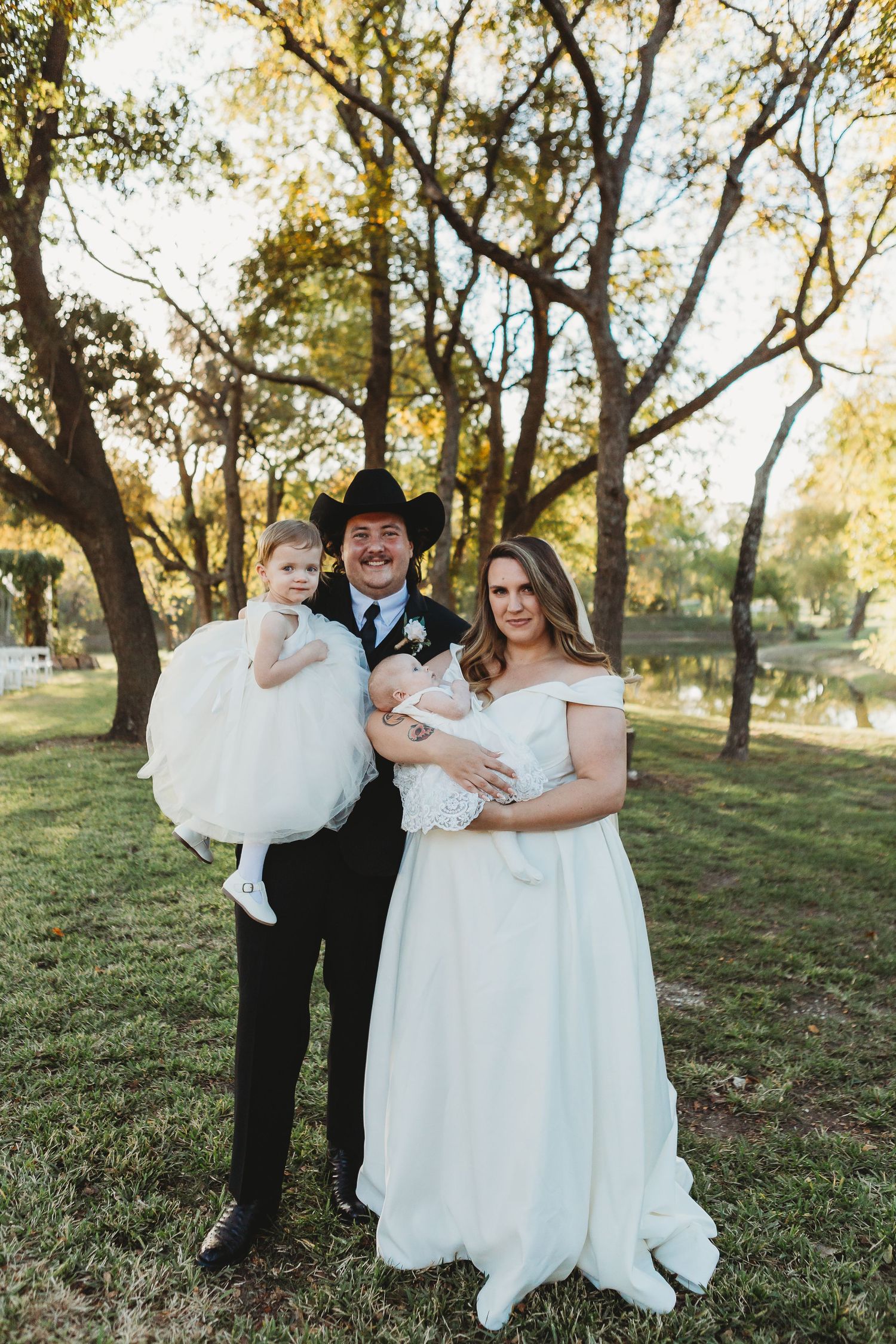 Newlyweds in western attire pose with young children during outdoor wedding ceremony.