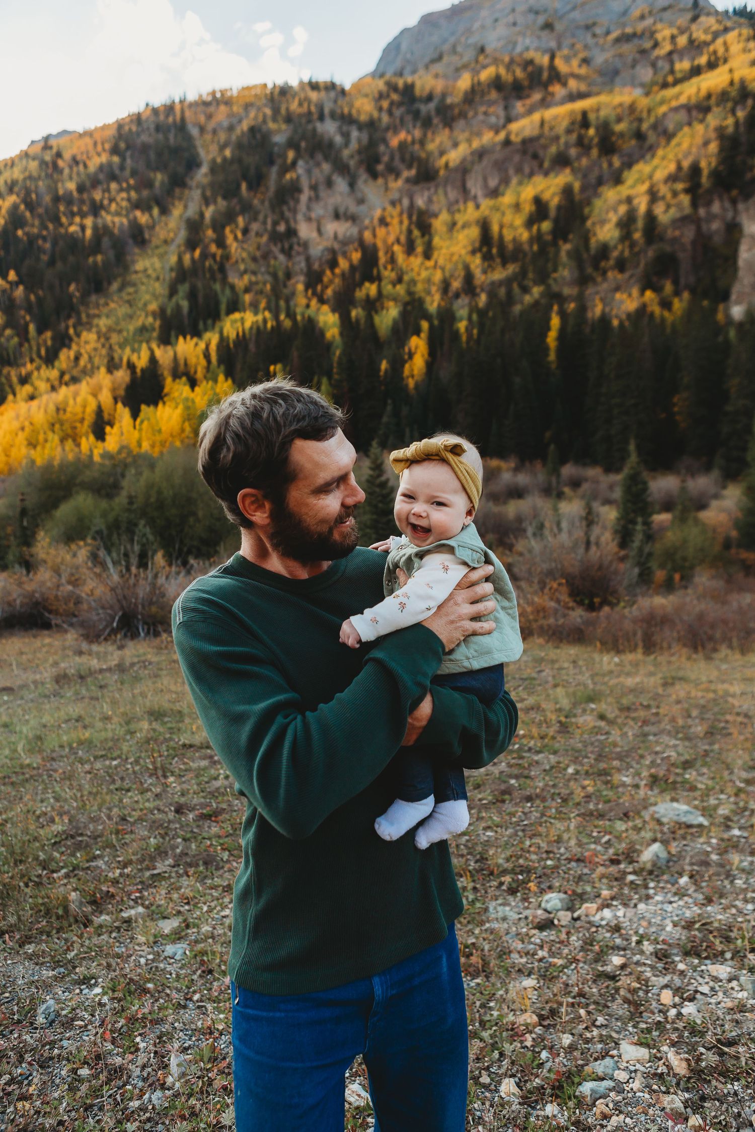 A parent and baby share a tender moment against a backdrop of autumn mountain scenery with golden aspen trees.