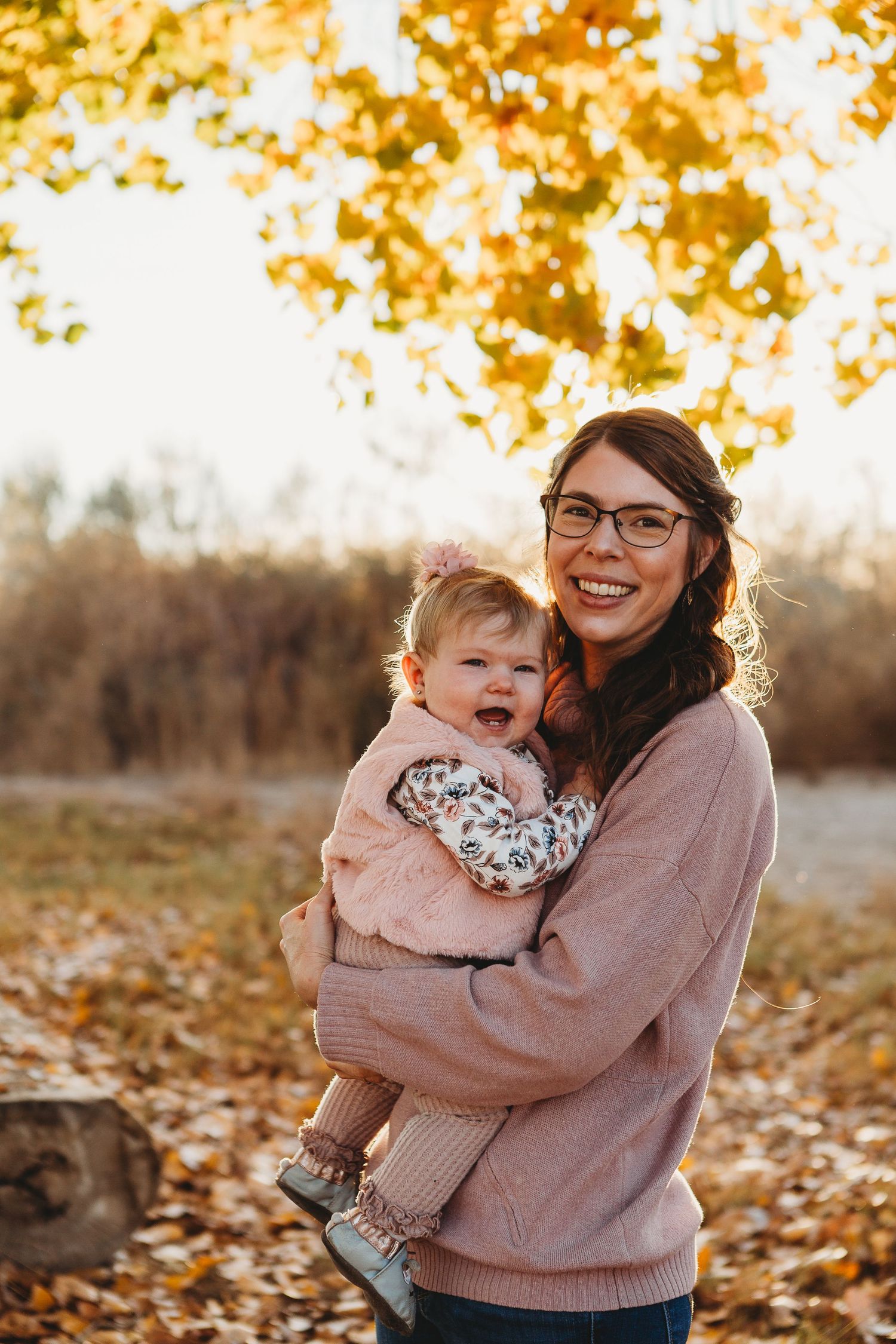 A cozy autumn moment captured with a baby in pink being held in a matching sweater outdoors.