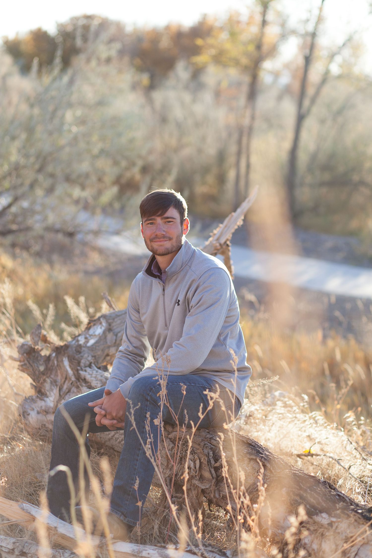 Person sitting outdoors in autumn sunlight surrounded by dry grass and golden light.