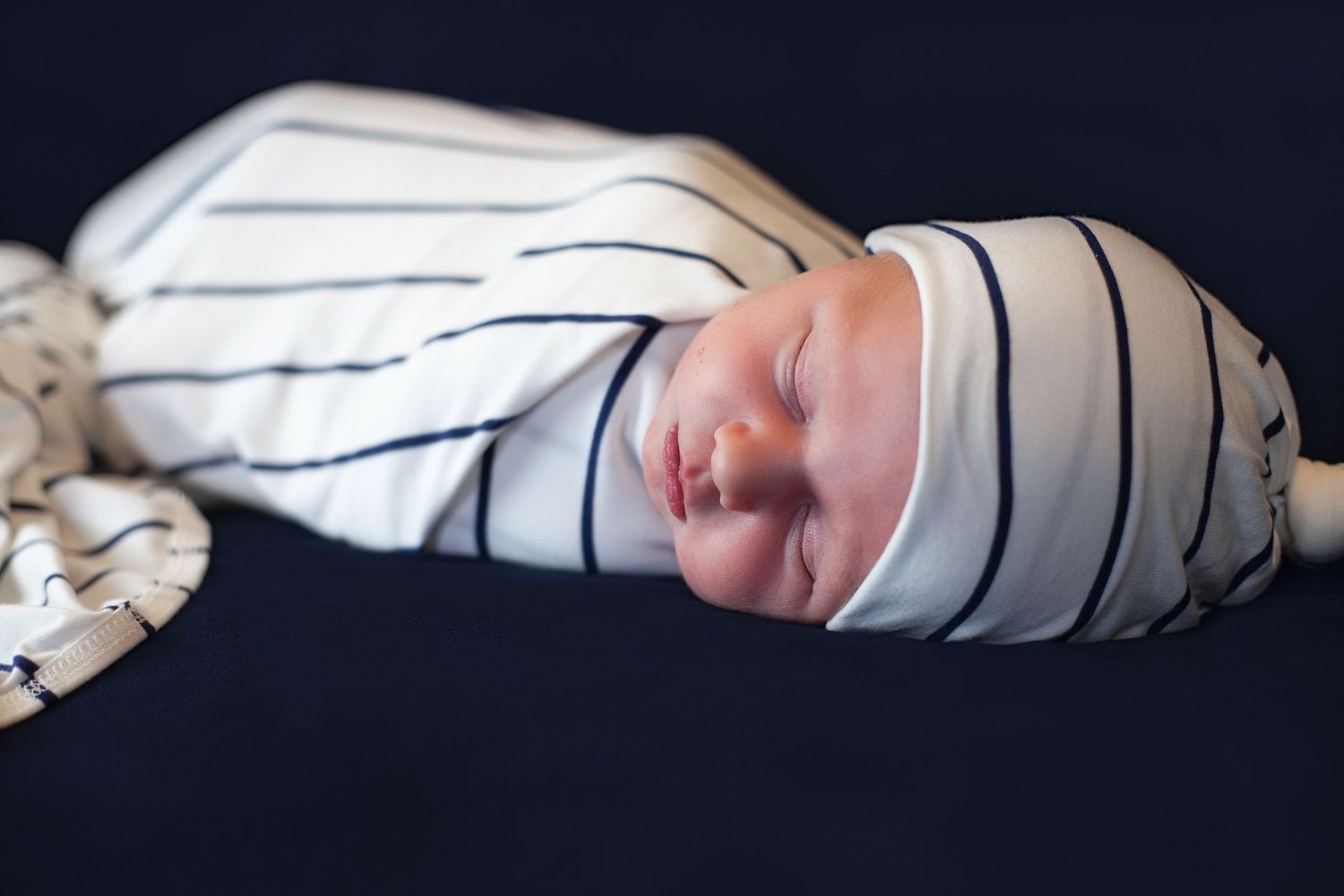 Newborn baby wearing striped sleepwear sleeping peacefully against dark background.