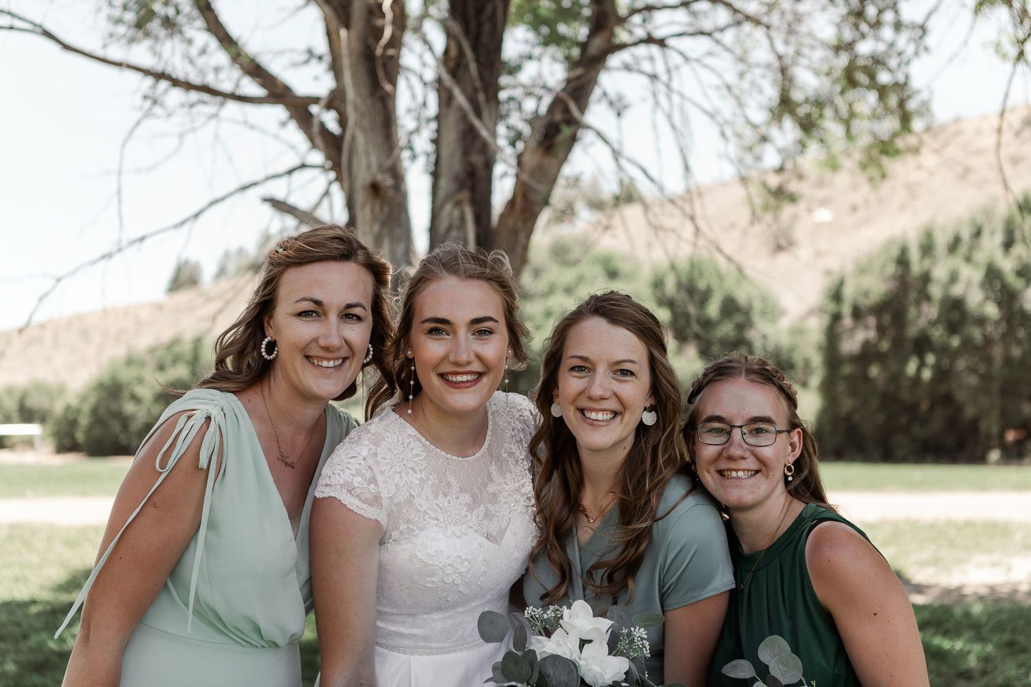 Wedding party posing together under a tree with bridesmaids in mint and emerald dresses.