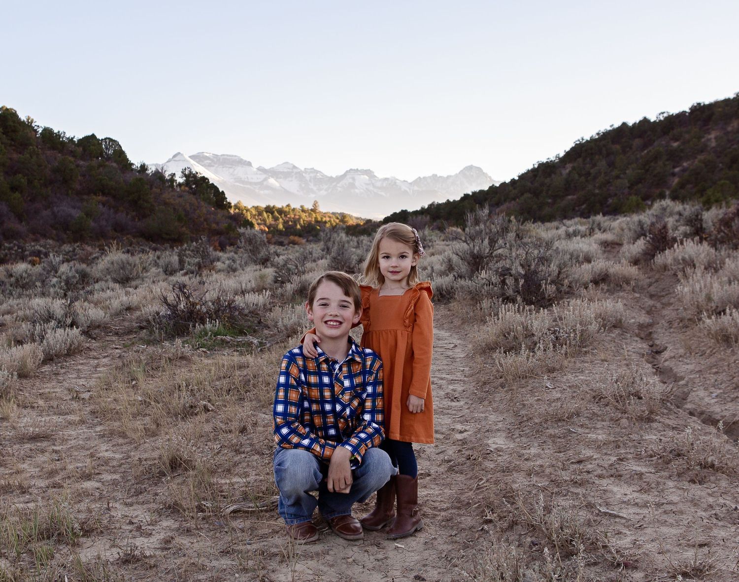 Two children pose together on a desert trail with mountains in the background.